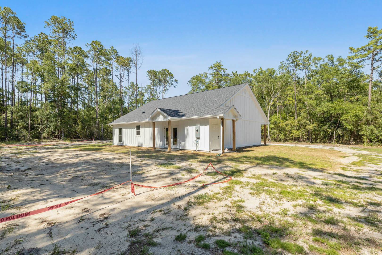 White house with grey roof, surrounded by a fenced area, red tape around a pole, grassy yard, and trees in the background.