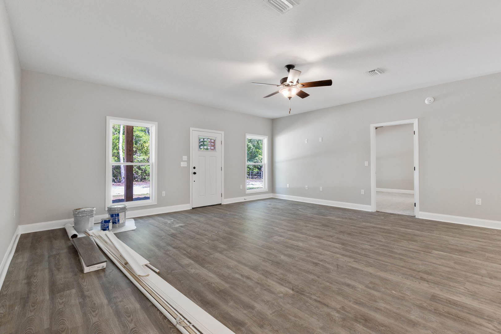 Hardwood floor room with ceiling fan, white walls, window framed by wooden post, white door featuring stained glass inset