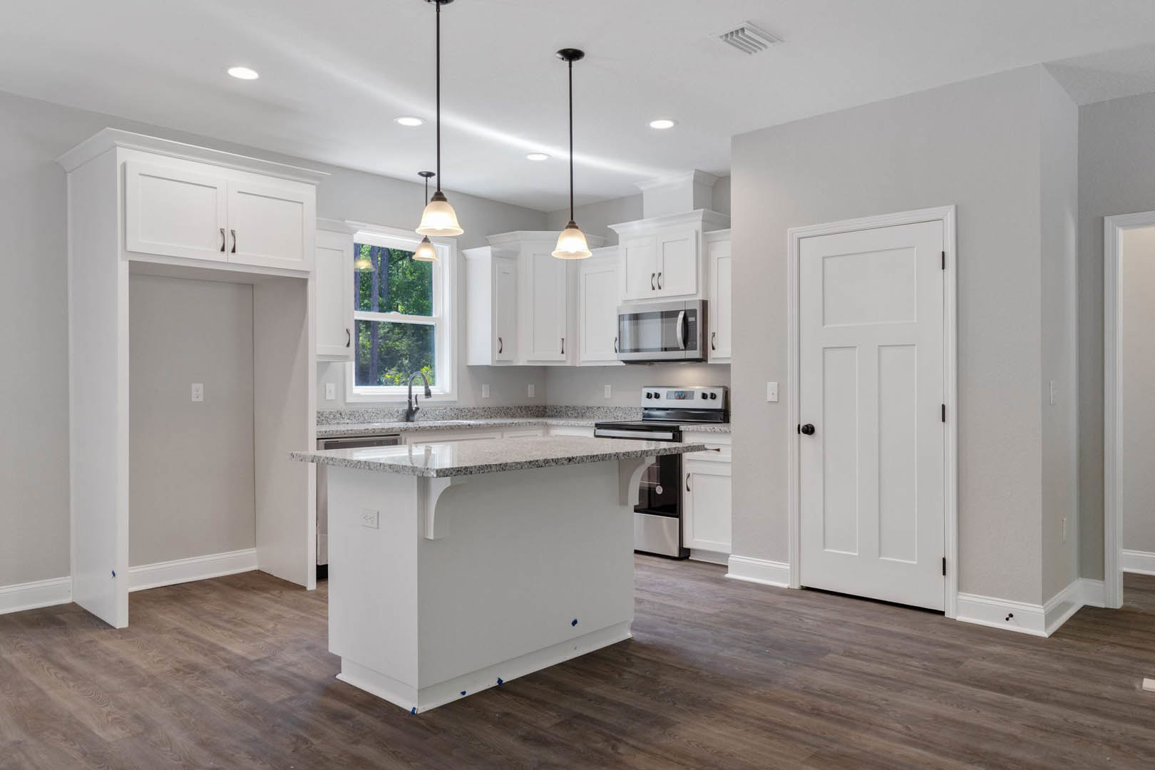White and black kitchen featuring a marble-topped island, wood flooring, white cabinetry with black knobs, built-in microwave with glass door, and pendant lighting above the