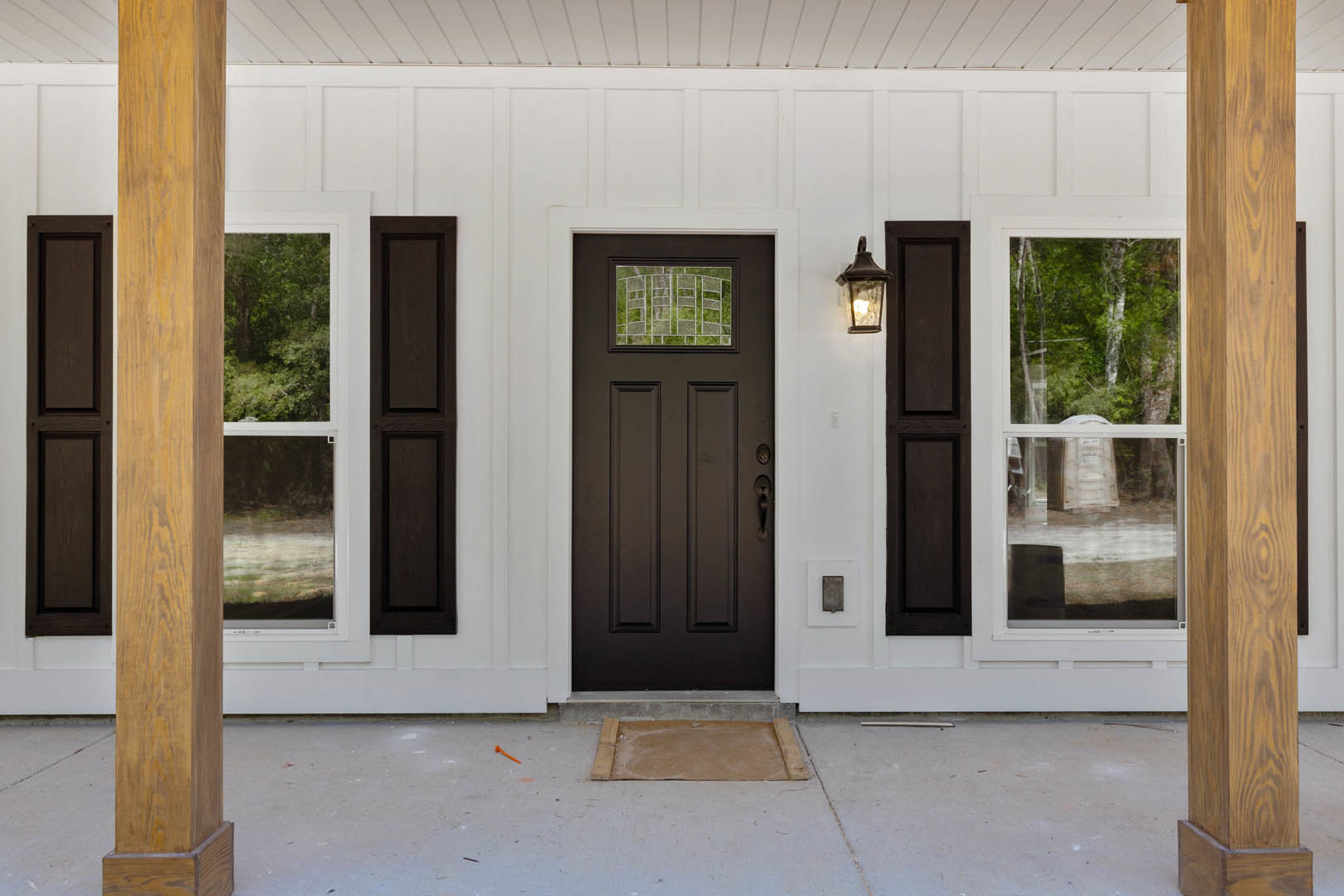 Black wood front door with white trim, brown siding, adjacent window, and light-colored entry floor