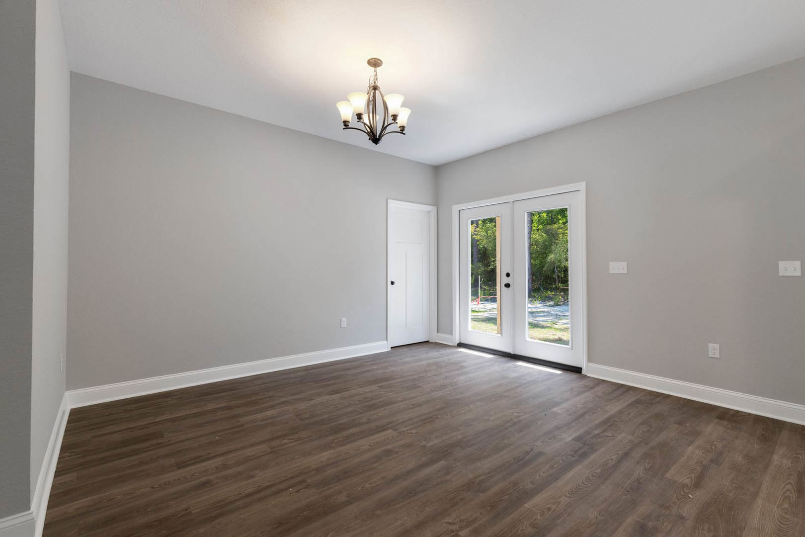 Hardwood floor room with white paneled door, black handle, double glass-paned doors, five-light chandelier, white walls, crown molding