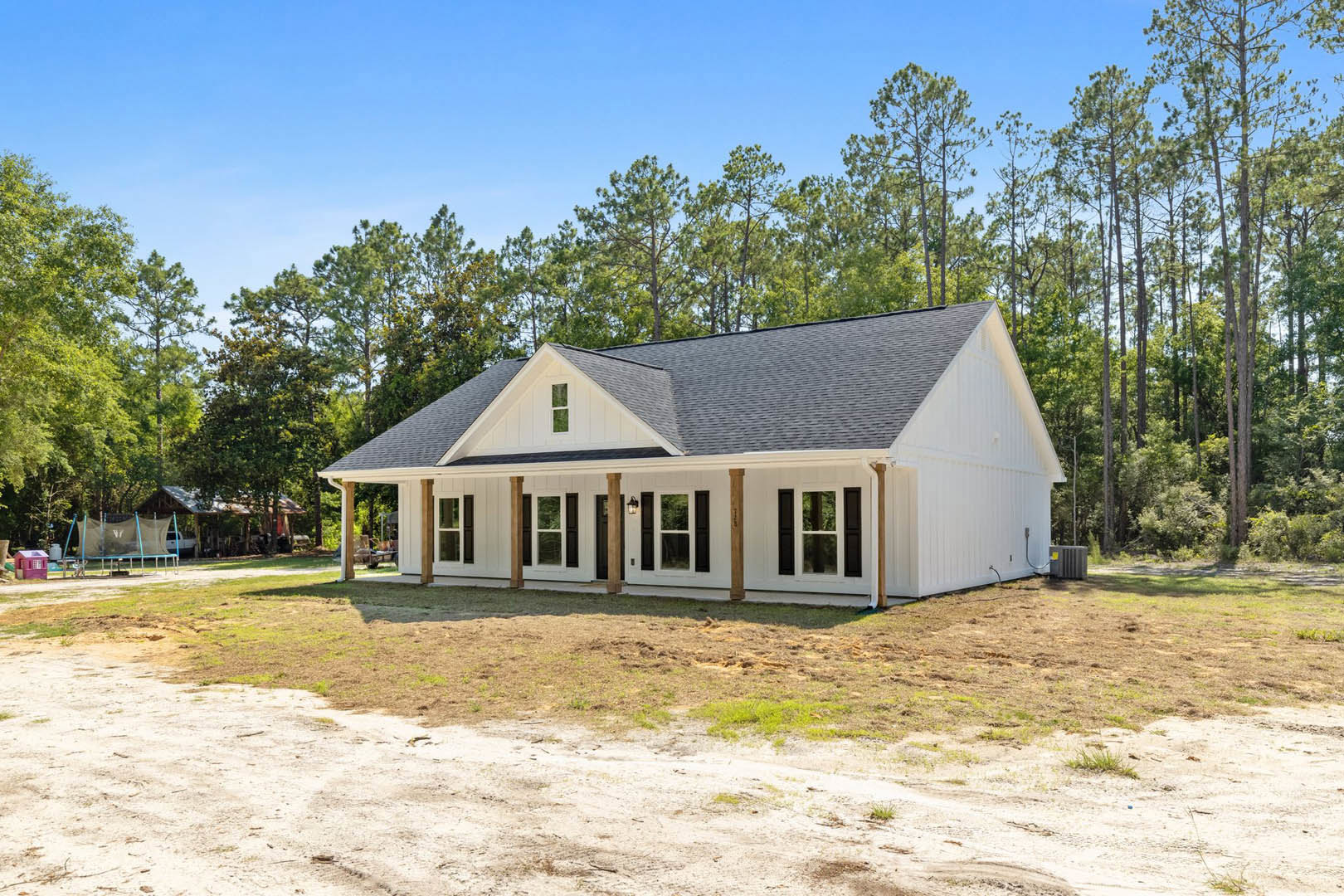 White house with black roof and shutters, dirt patch in front, trees and Little White House visible in background, white-framed window, grey utility box with yellow label near
