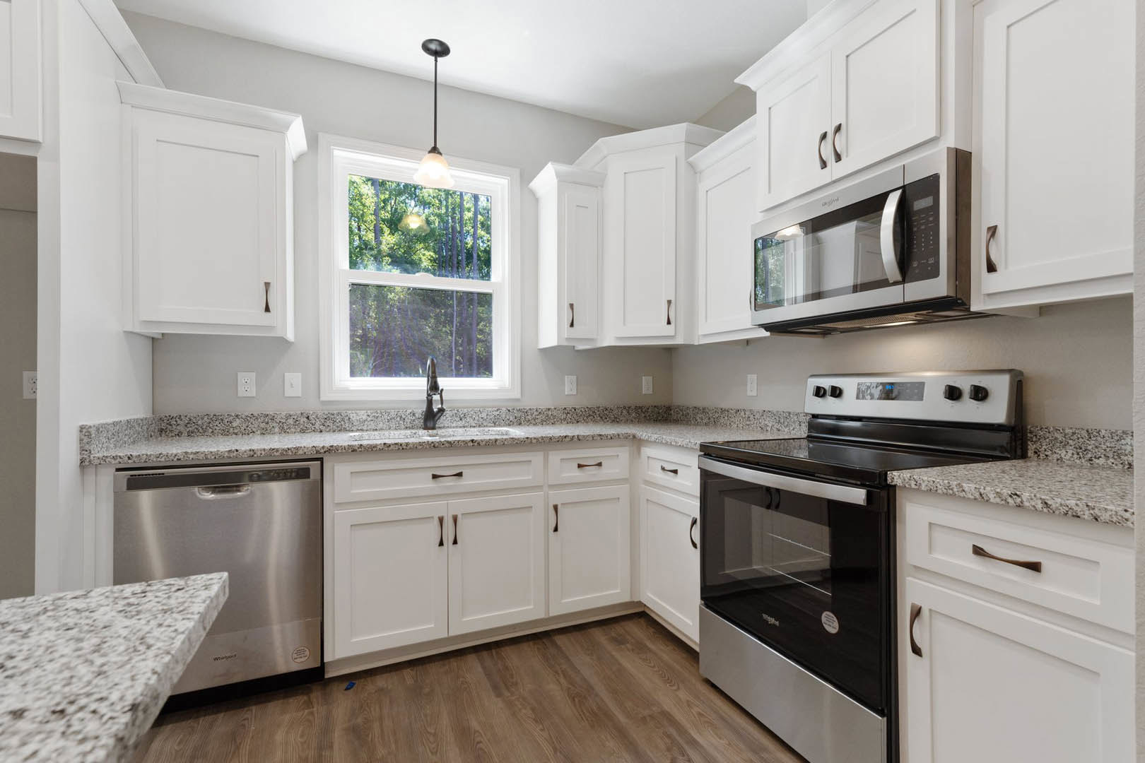 White shaker cabinets, stainless steel stove and oven, built-in microwave, quartz countertop, stainless steel dishwasher, window overlooking trees
