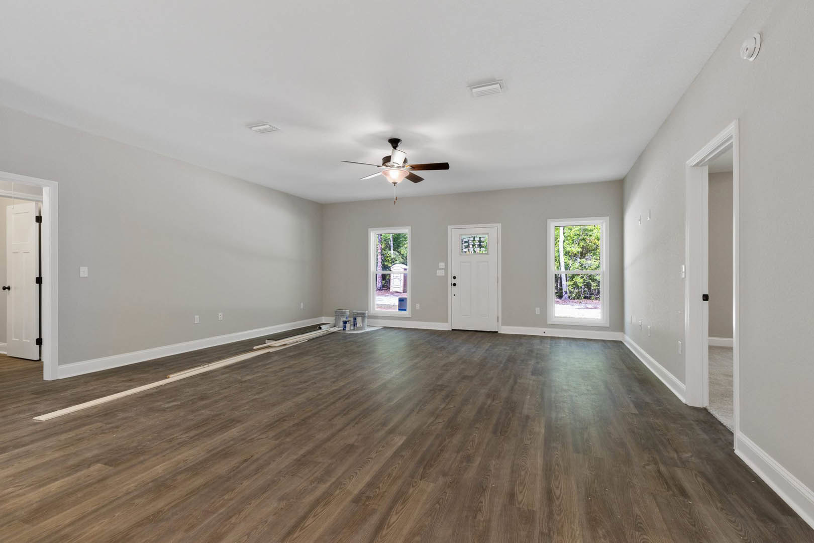 Hardwood floor room with ceiling fan, white door featuring stained glass window, large window showing trees outside, white object resting on white surface