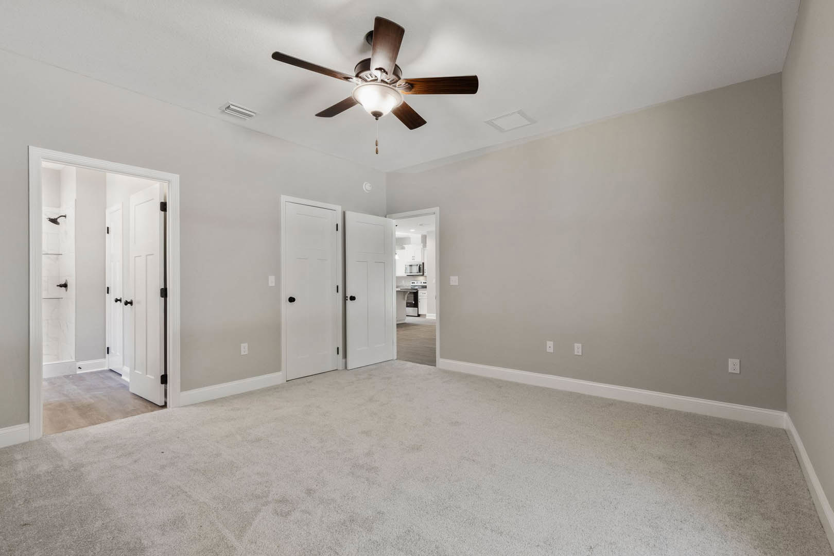 Carpeted room with white walls, ceiling fan with light fixture, white doors with black knobs, partial view of bathroom with shower
