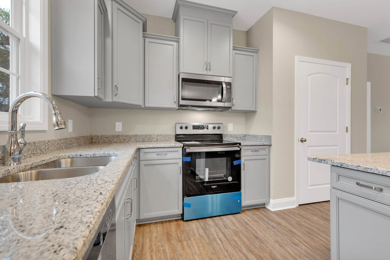 Granite countertops with wood cabinetry, stainless steel oven and microwave, chrome faucet above a deep sink, white door visible in kitchen interior