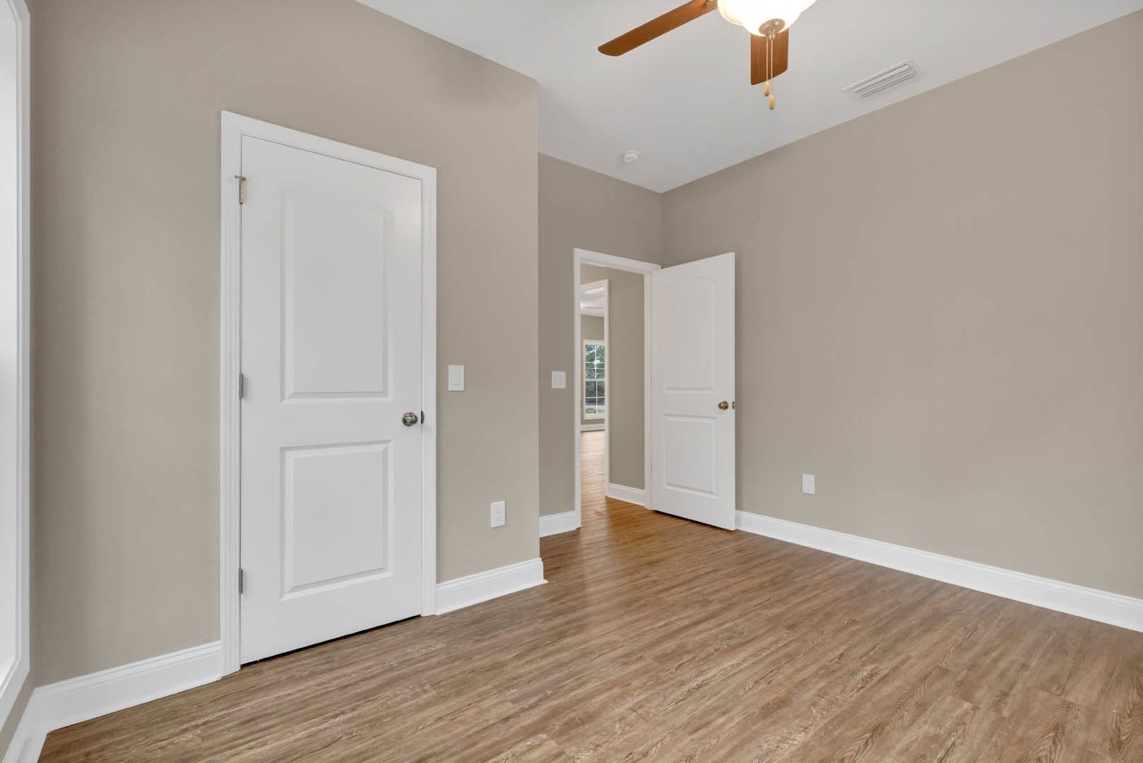 Room with two white paneled doors featuring silver and gold knobs, hardwood floor with white baseboard trim, ceiling fan overhead
