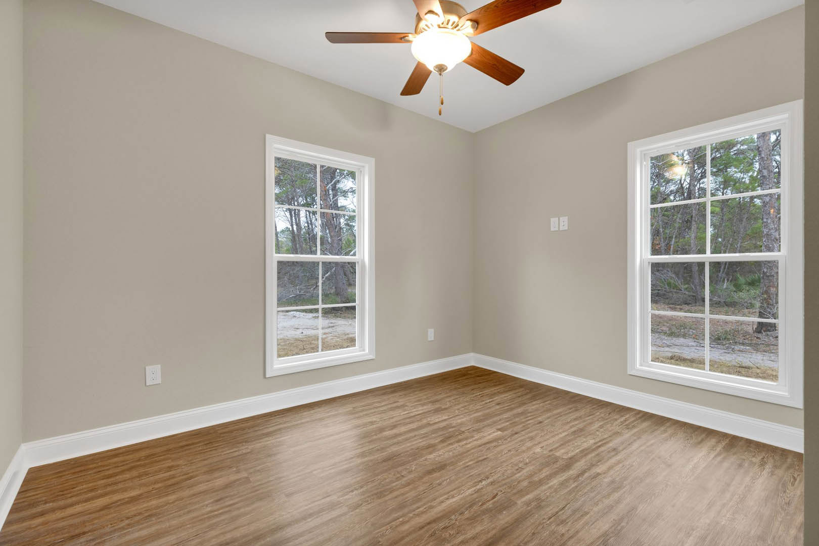 Ceiling fan with light fixture, large windows showing trees outside, wood flooring, white walls, crown molding