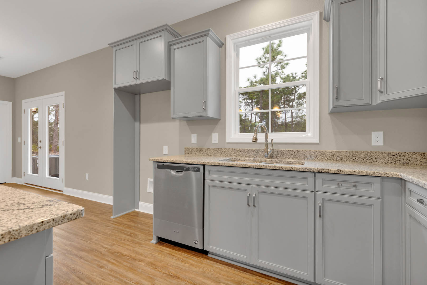 Grey shaker cabinets and silver refrigerator in a kitchen with white countertops, a window overlooking trees, and a glass-paneled door.