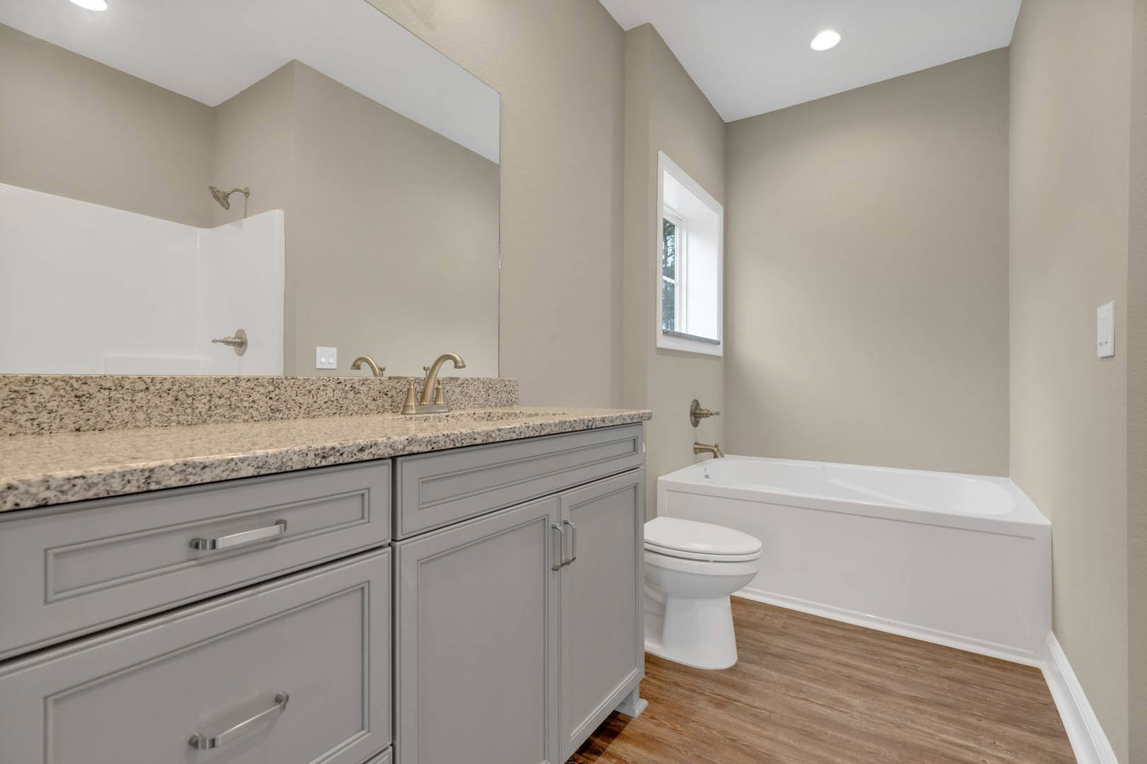 Bathroom with white bathtub beside toilet, white sink set in stone countertop, tile flooring, cabinetry with metal handles, and white door with glass window