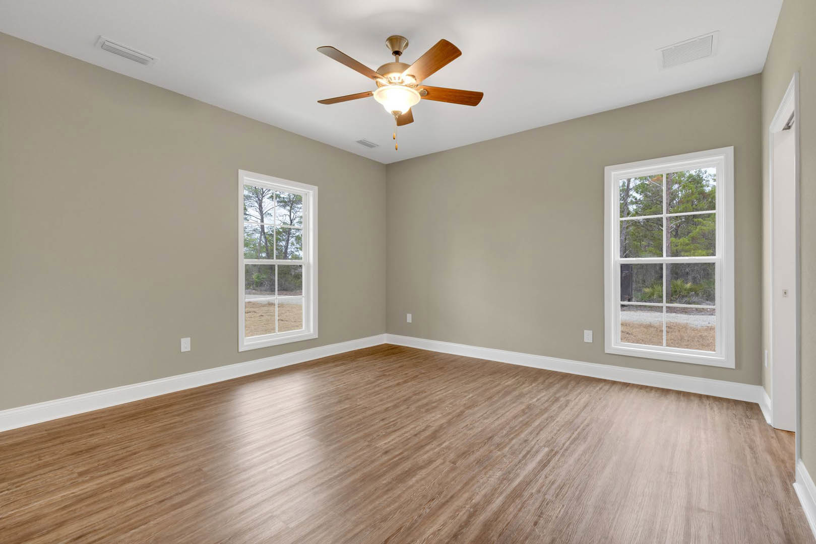 Wood flooring in a bright room with large windows overlooking trees, ceiling fan with light fixture centered above
