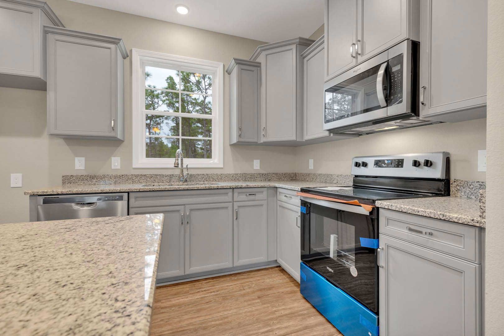 Granite countertops with white cabinetry, stainless steel microwave, stove with blue drawer, window overlooking trees, close-up of counter and white door