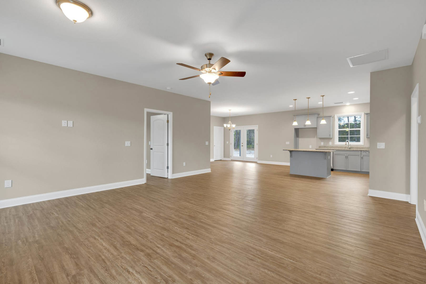 Spacious living room with hardwood flooring, ceiling fan with light, white walls, double glass-panel doors, and a white door with metal handle