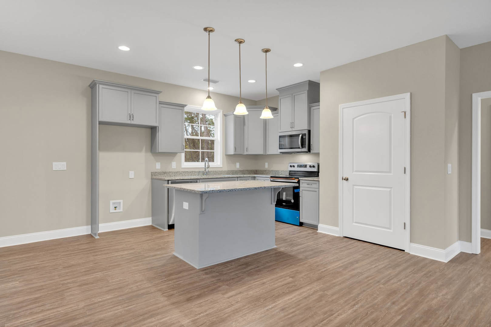 Kitchen with marble-topped island, wood flooring, white cabinetry, stainless steel microwave, silver door knob on white door, white walls, and sink.
