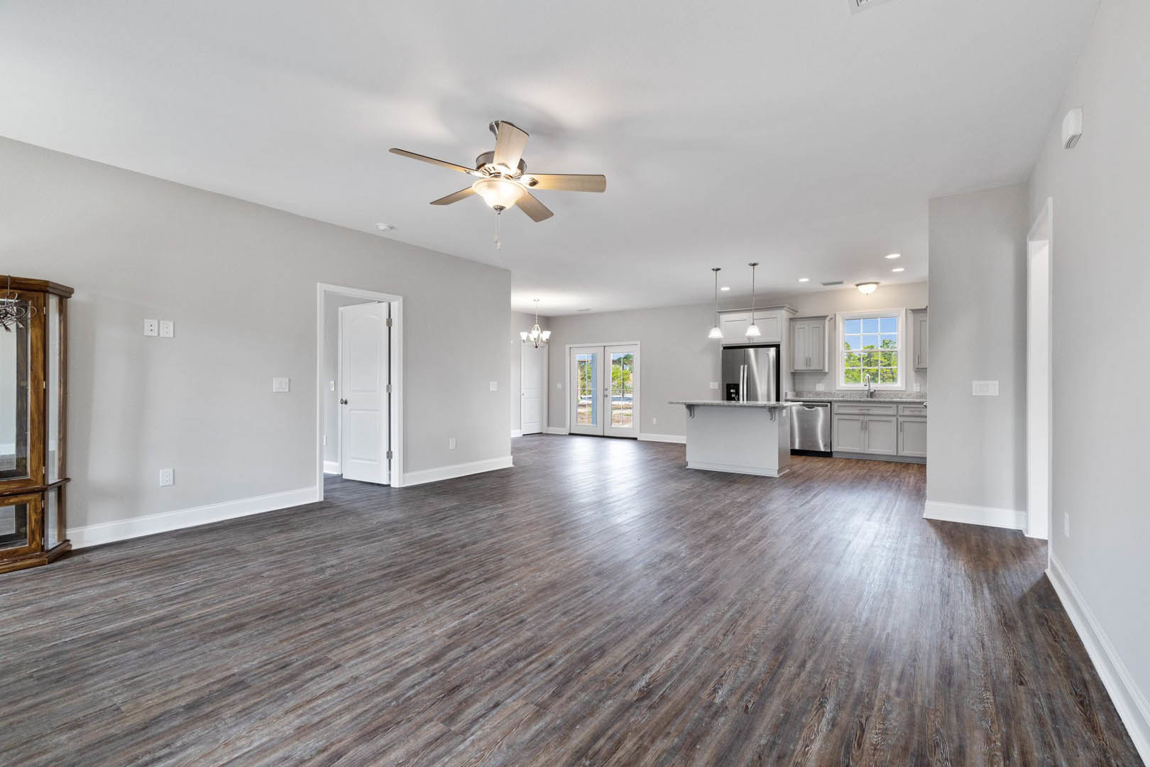 Spacious open floor plan featuring hardwood flooring, ceiling fan with light, wooden post beside glass door, white door with silver handle, and stainless steel refrigerator with