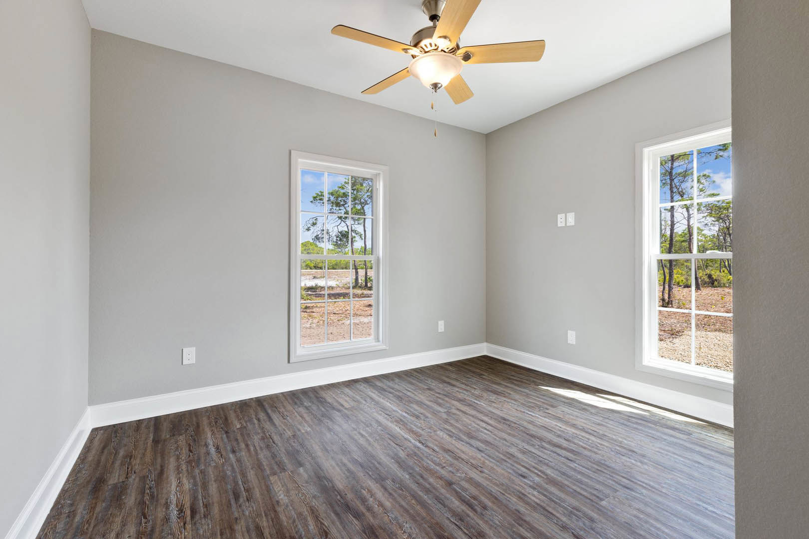 Ceiling fan with light fixture mounted on white plaster ceiling, wood flooring, large windows with tree views, simple wall molding
