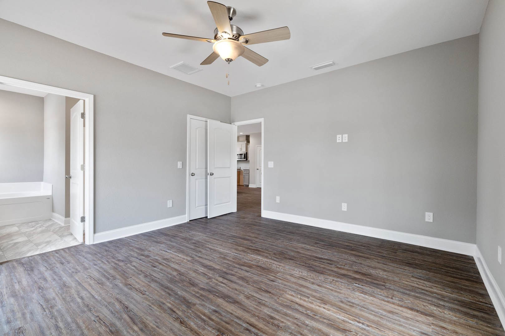 Ceiling fan with light fixture mounted on white ceiling, wood flooring, white paneled doors with silver knobs, neutral walls