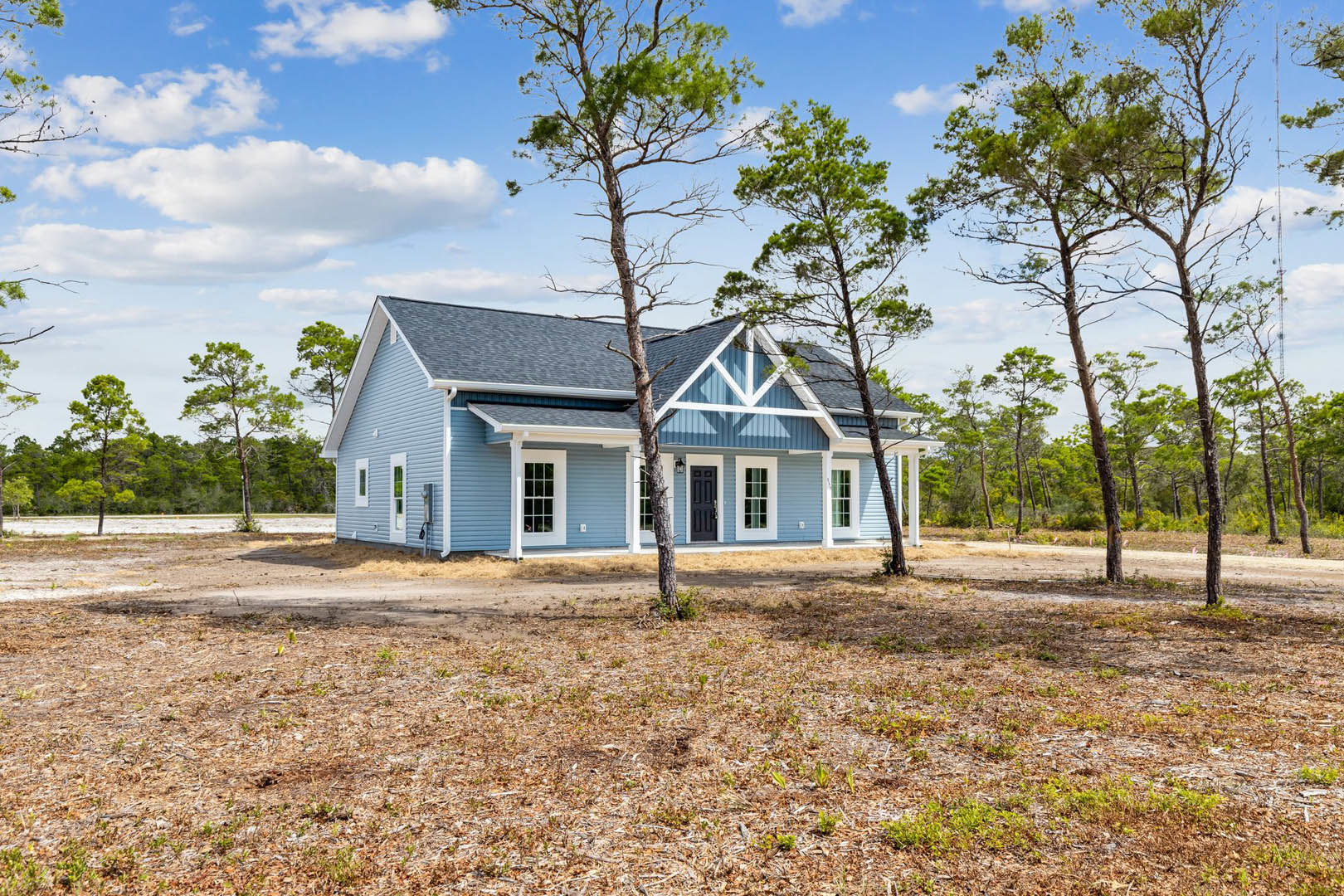 Two-story cottage-style home with multi-pane windows, surrounded by leafless trees and grassy lawn under a cloudy sky