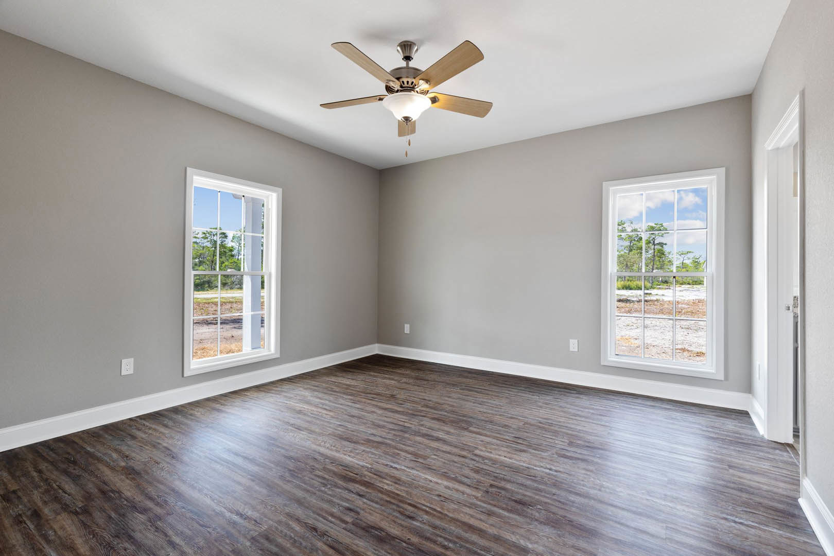 Ceiling fan with light fixture, wood flooring, large windows overlooking forested landscape, white plaster walls
