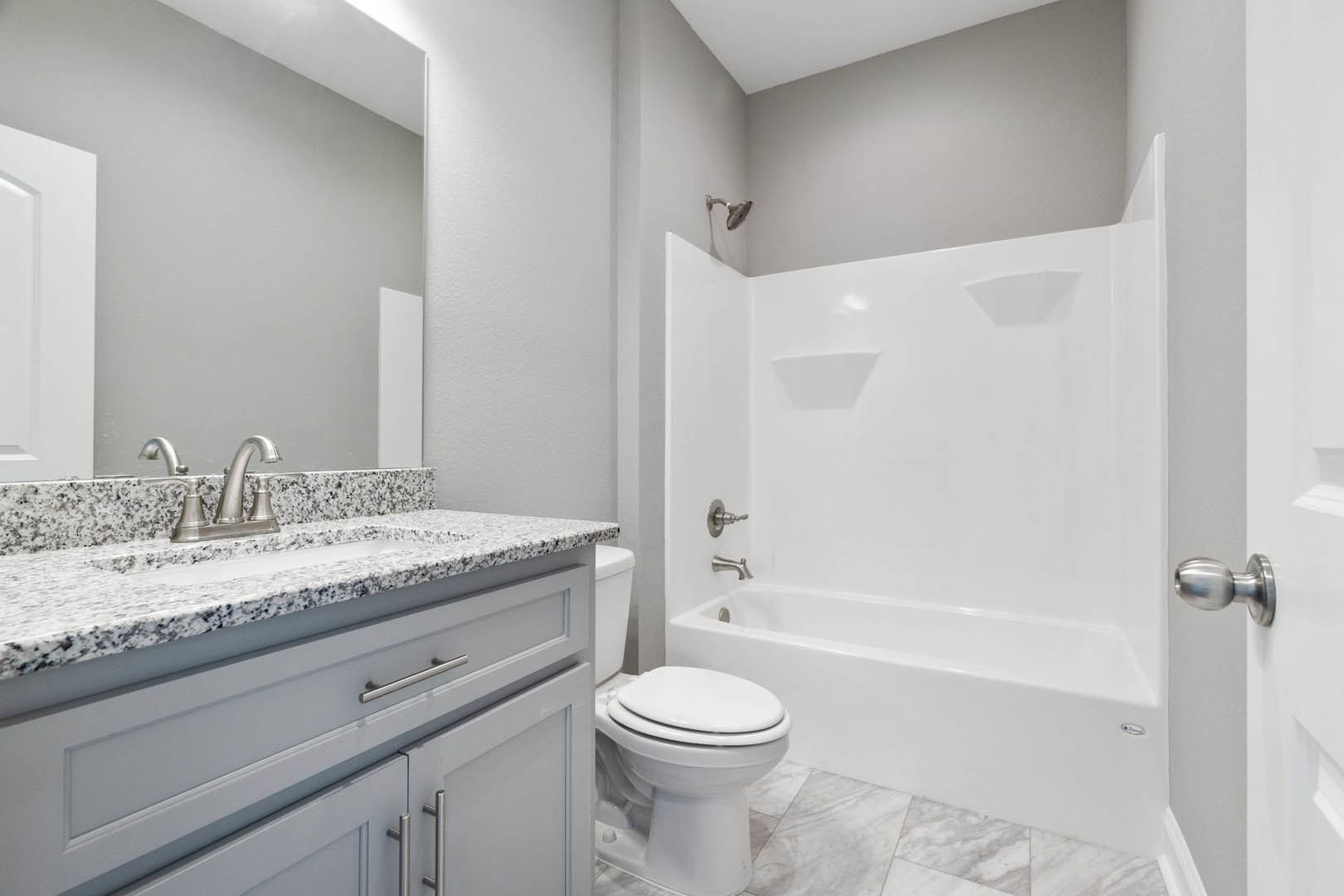 White freestanding bathtub and modern toilet on gray tile floor, light wood vanity with vessel sink, chrome faucet, and neutral tiled walls