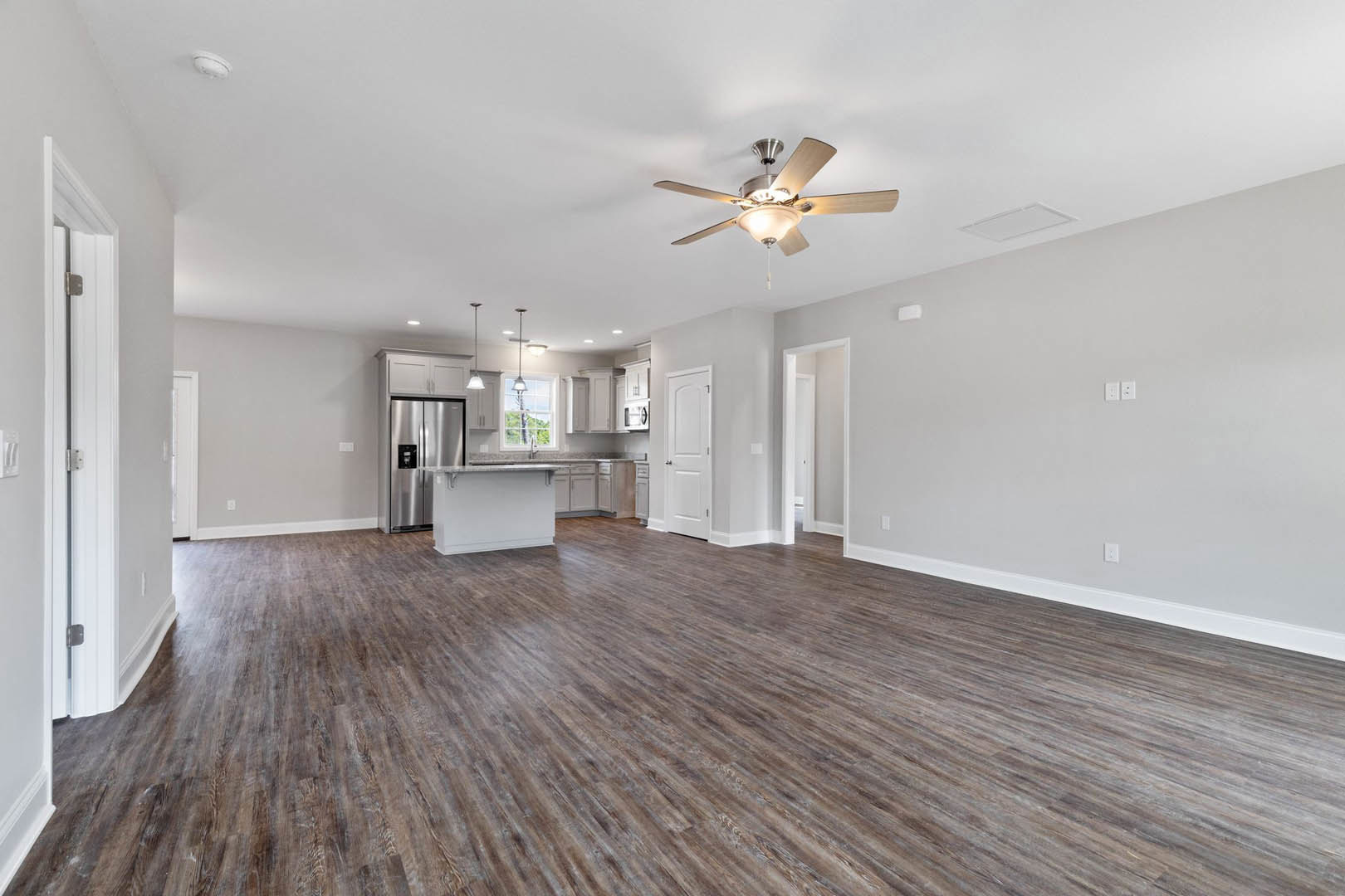 Open-concept kitchen with wood flooring, white countertops, stainless steel refrigerator, ceiling fan with light fixture, and white door with black handle