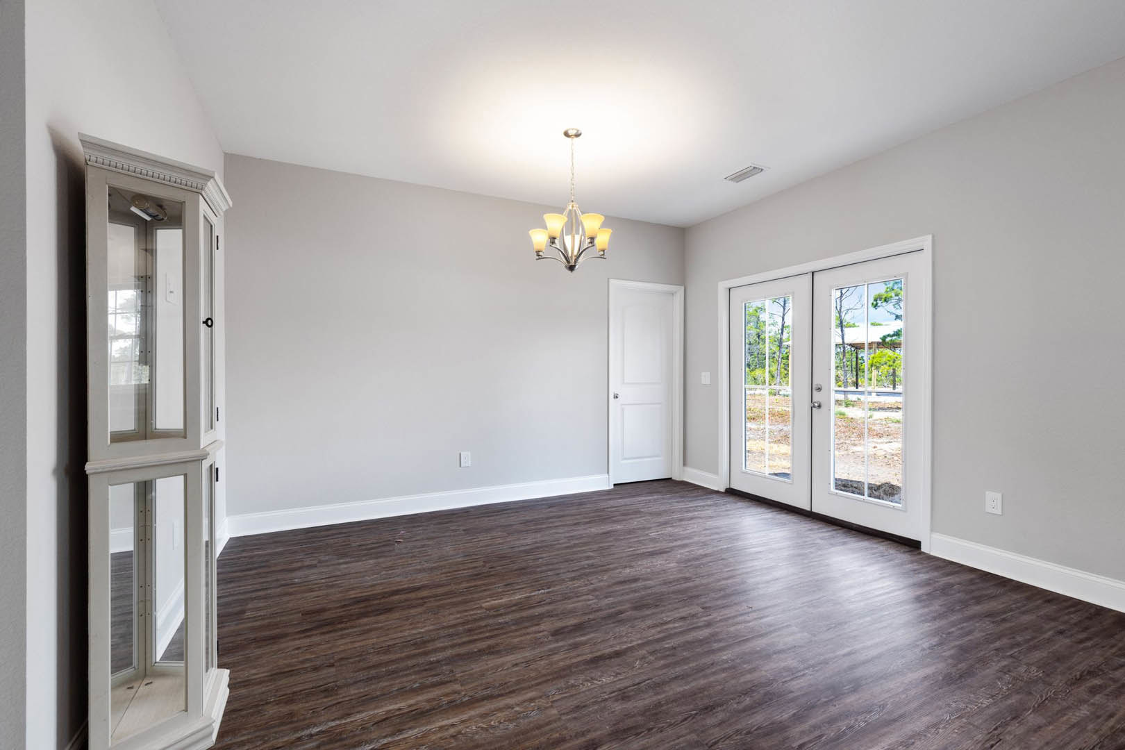 Wood flooring in a spacious room with double white doors featuring glass panels and a silver handle, illuminated by a decorative chandelier.