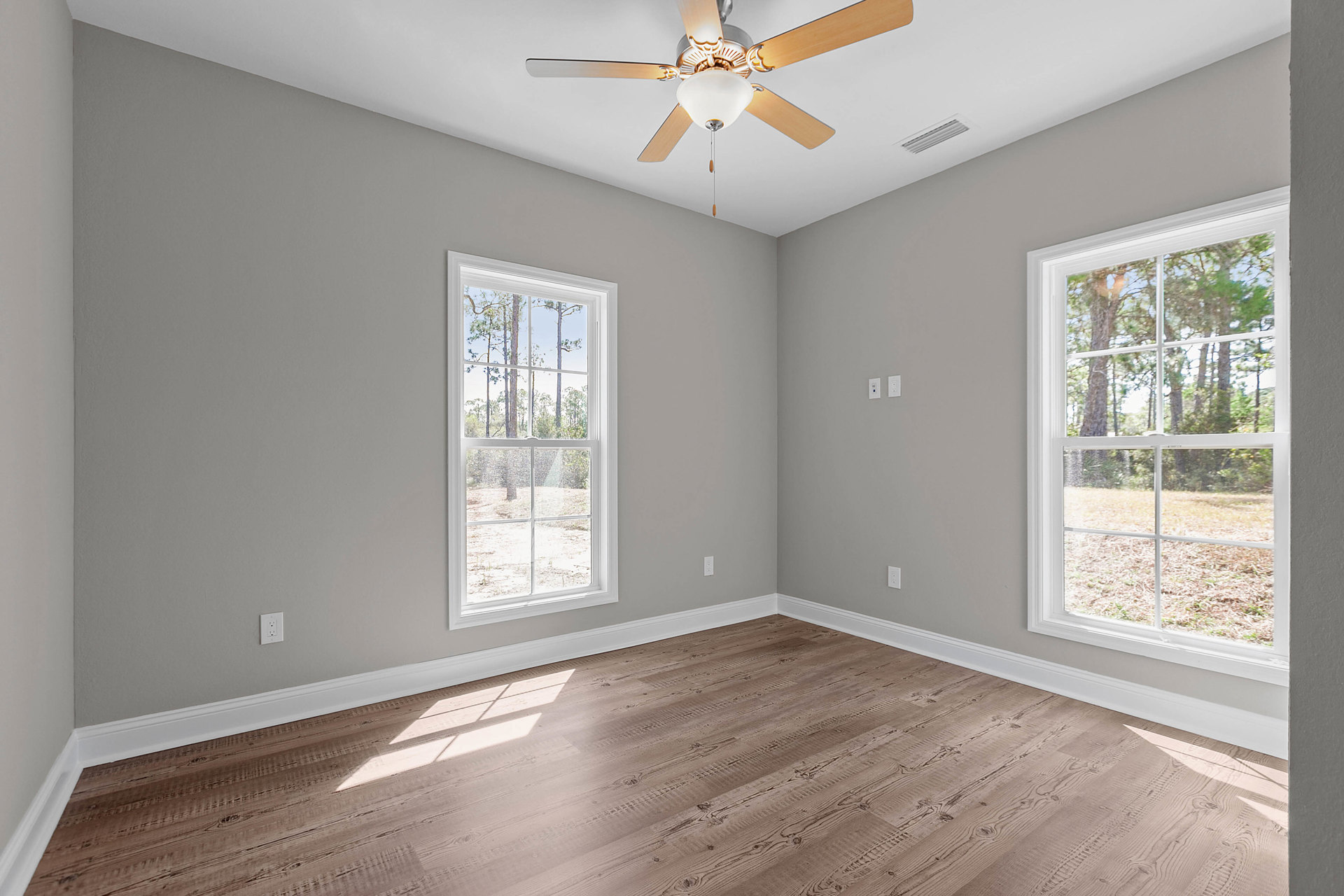 Ceiling fan with light fixture mounted on white plaster ceiling, large windows with black trim overlooking trees, wood flooring, white walls with decorative molding