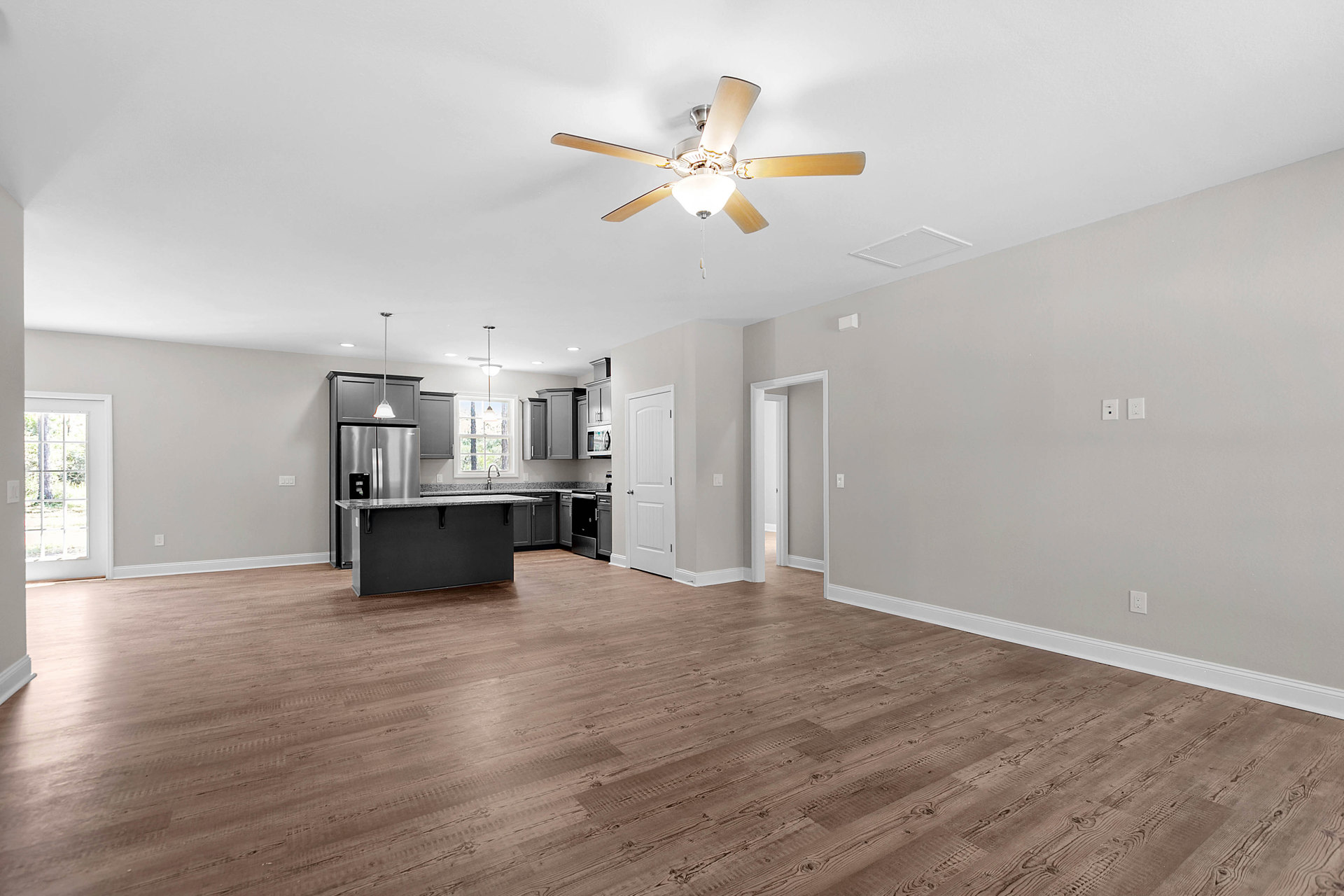 Open kitchen with wood flooring, white cabinetry, stone countertops, ceiling fan with light fixture, window overlooking outdoors, and white door with silver handle