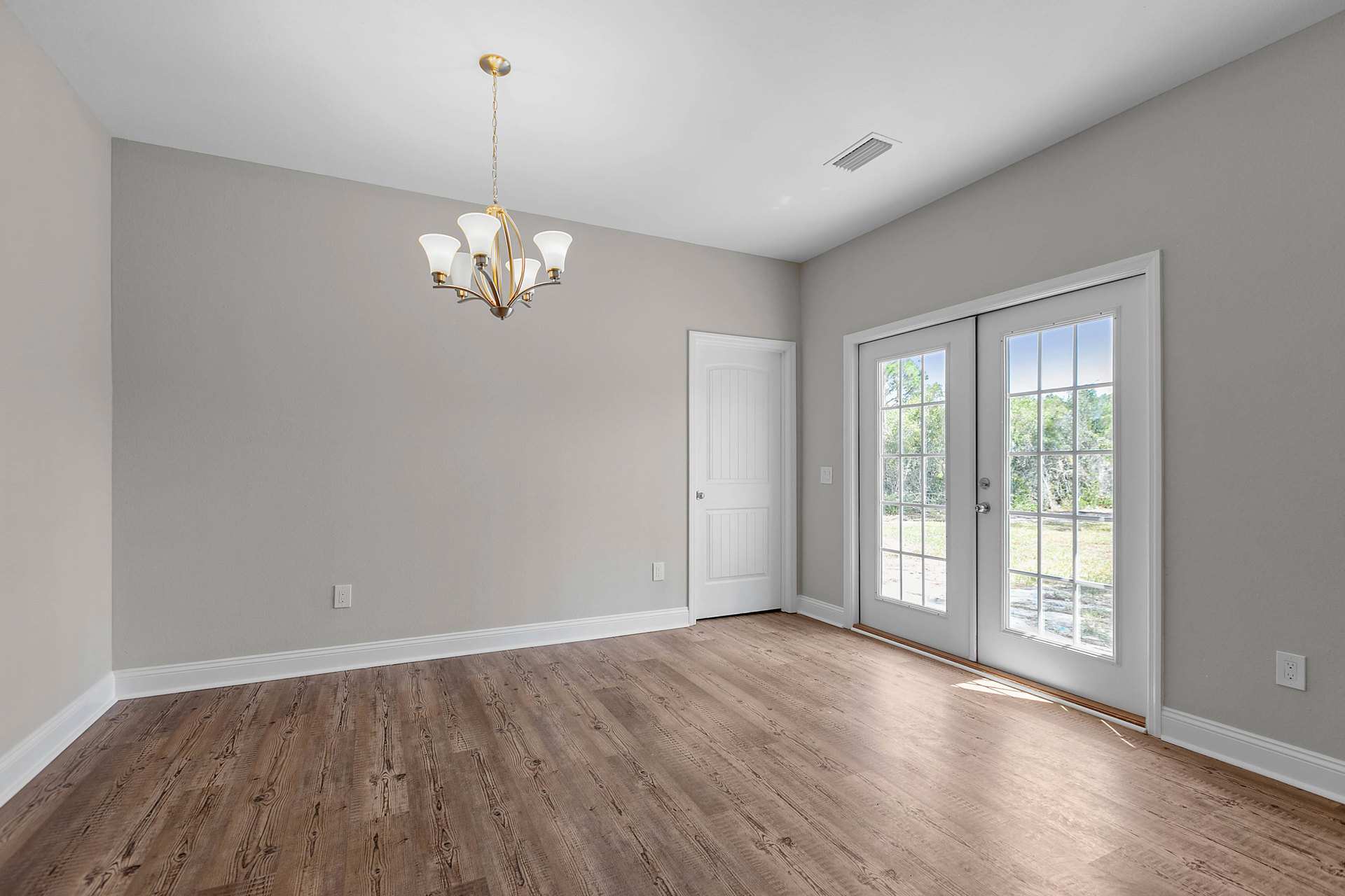 Chandelier with white shades hanging from a white ceiling, wood flooring with white trim, white door featuring a silver handle, ceiling vent, and light-colored walls.