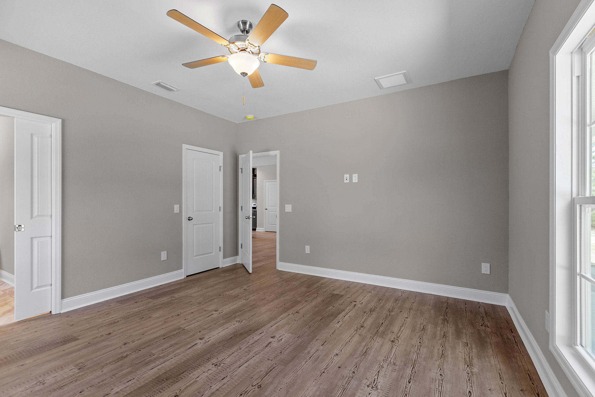 Ceiling fan with light fixture mounted on white plaster ceiling, wood laminate flooring with white baseboard trim, white door featuring silver handle, air vent in ceiling