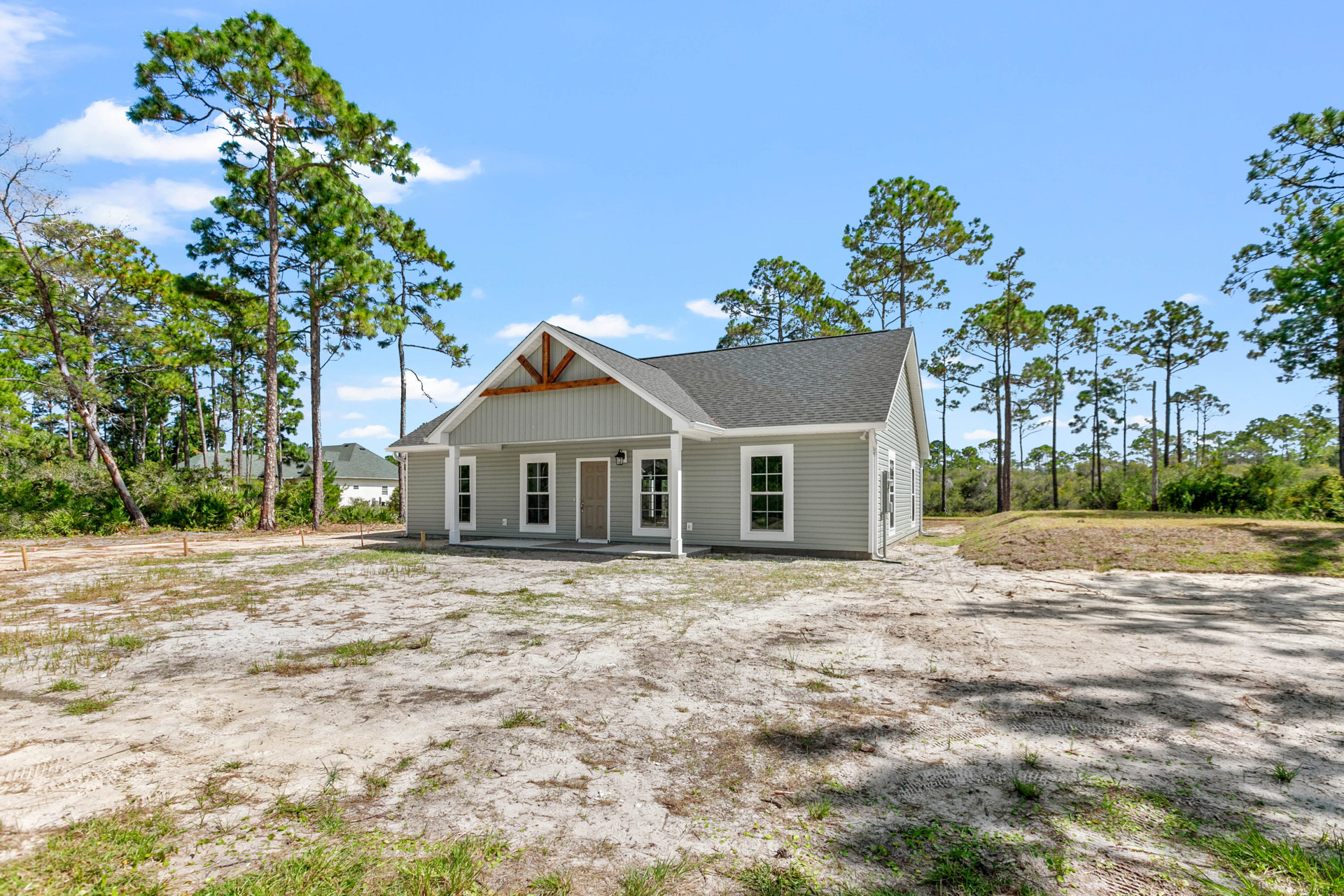 Two-story home with white siding, covered front porch, dark front door, fenced grassy yard, mature trees and blue sky in the background