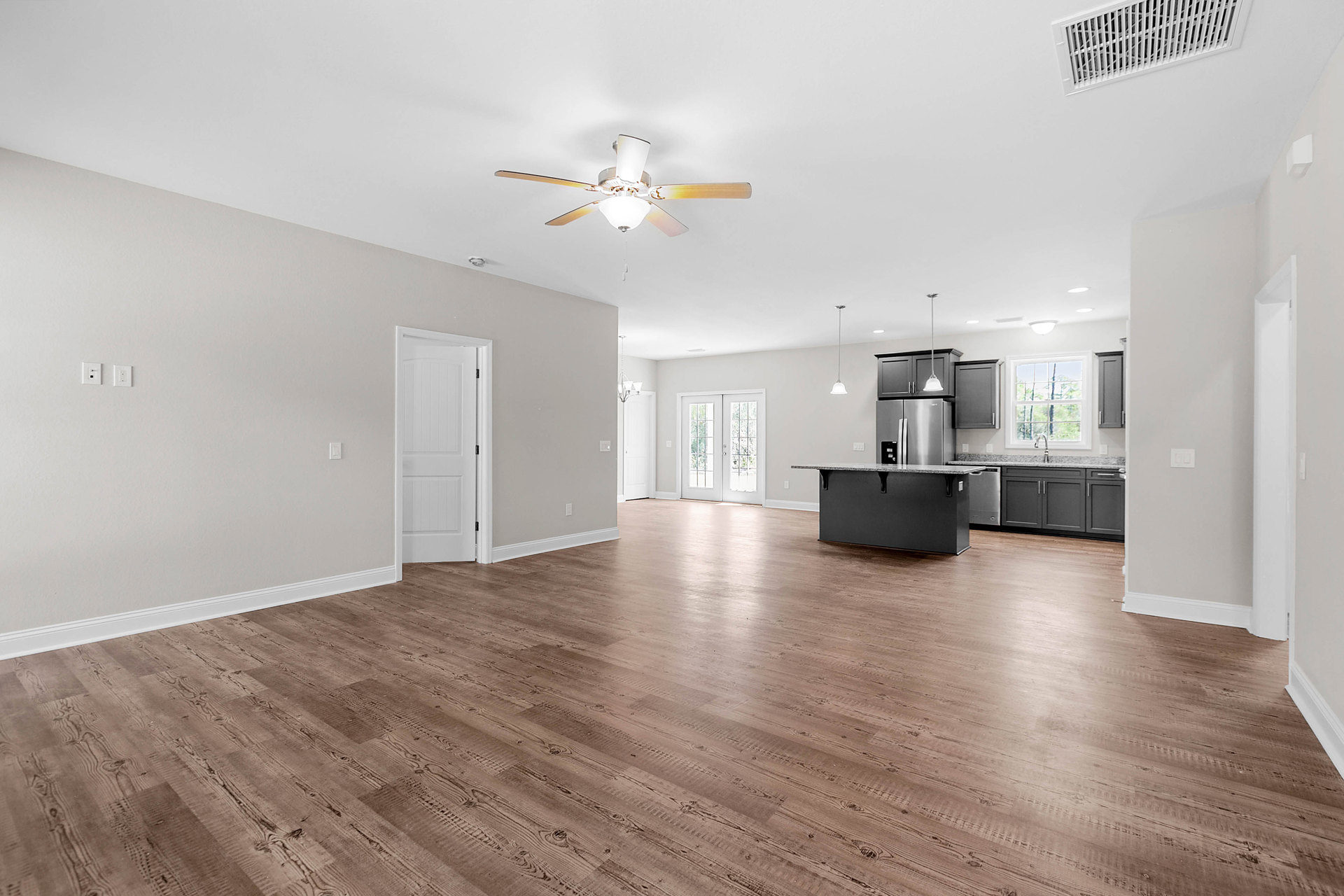Open-concept kitchen with white walls, wood flooring, central island, ceiling fan with light, white doors including double glass-paneled doors, and black hardware accents