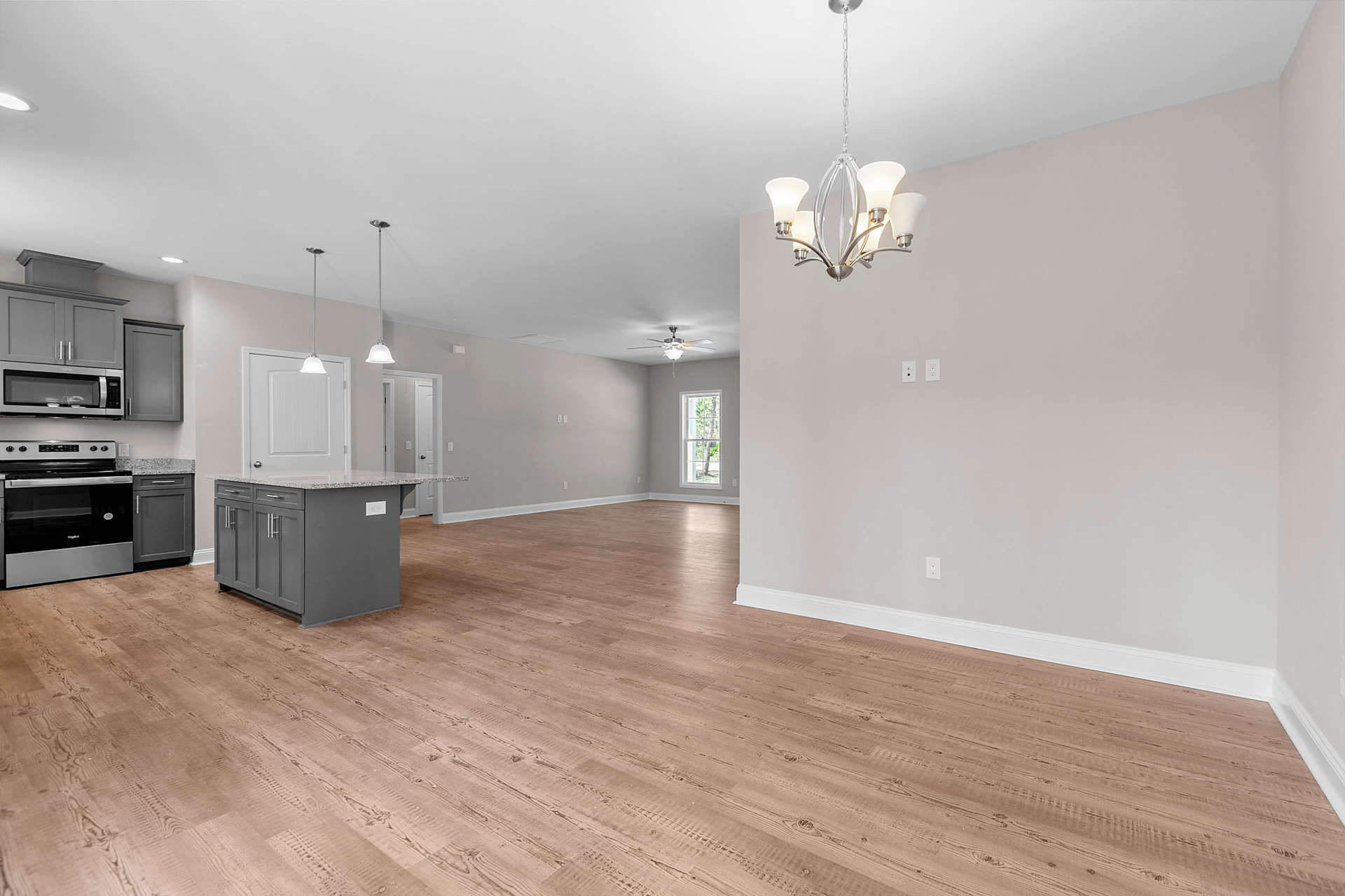 Kitchen with hardwood flooring, granite-topped island, stainless steel stove with glass door, four-light ceiling fixture, large window overlooking trees, white cabinetry, plaster