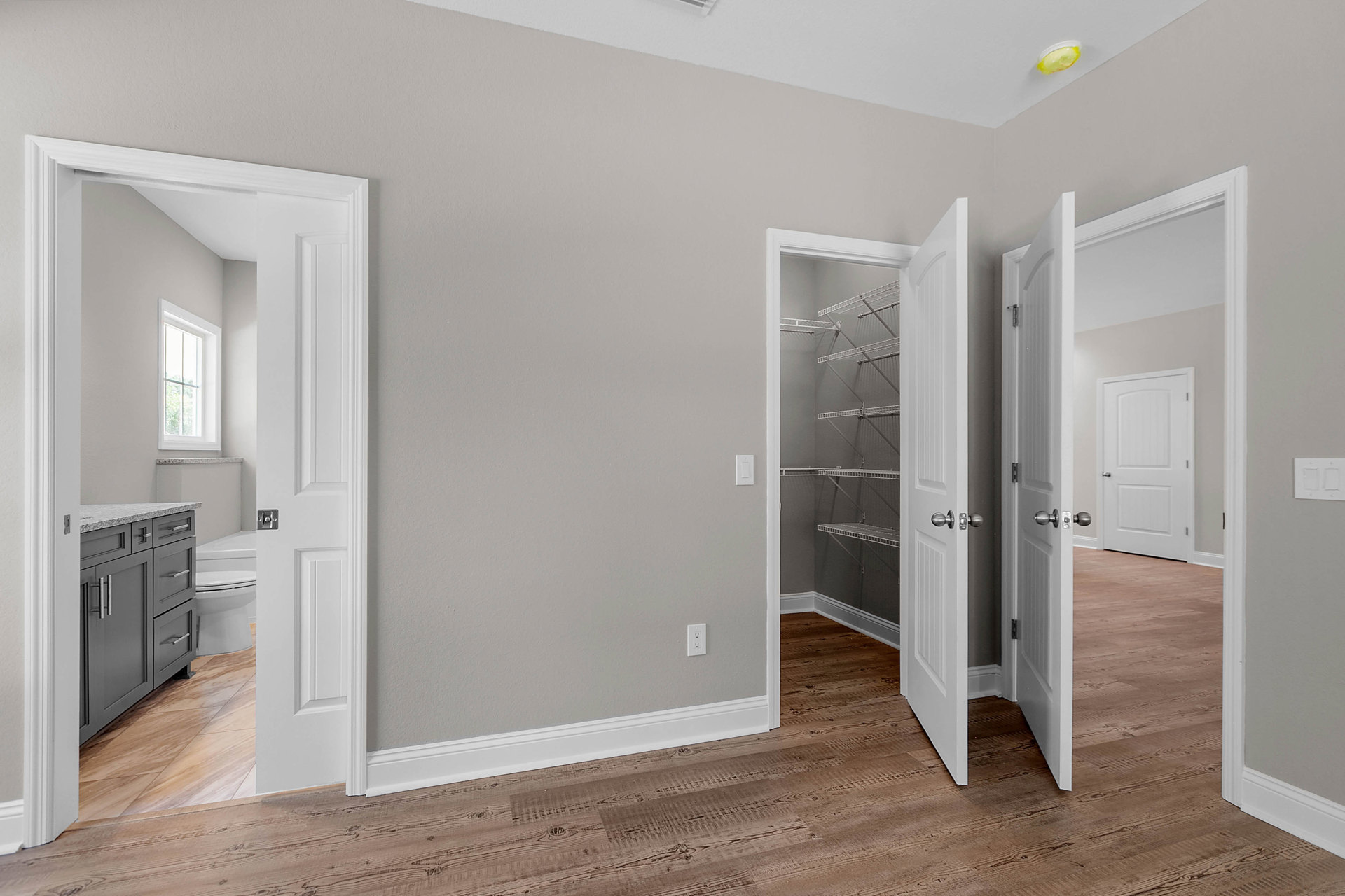 Open doorway leading to a room with light wood flooring, white walls, silver hardware on doors, white cabinetry, and a visible toilet with lid up.