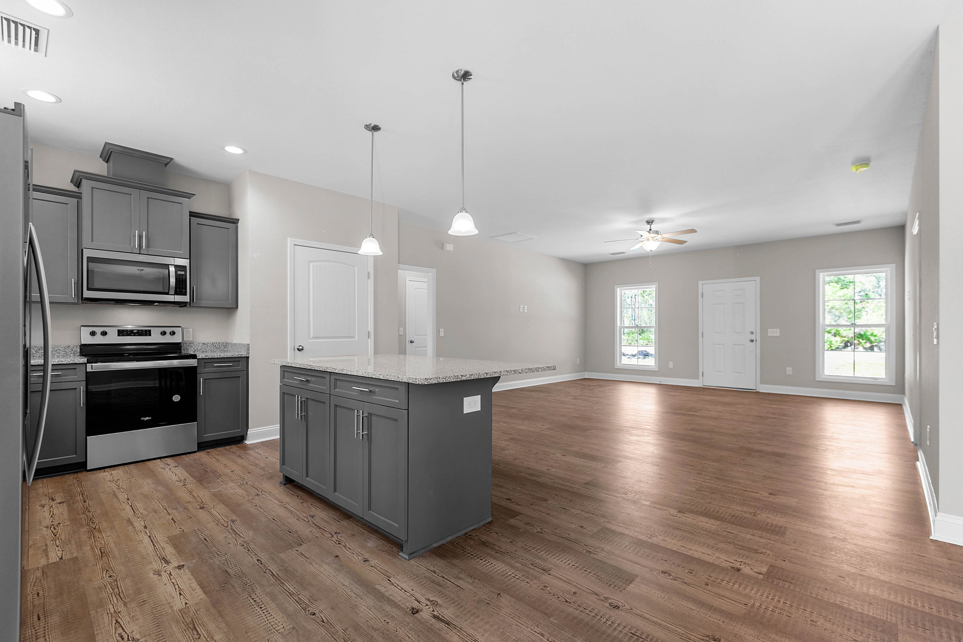 Open concept kitchen and living room featuring hardwood flooring, white cabinetry, stainless steel microwave, stove and oven, kitchen island with wood floor, window overlooking