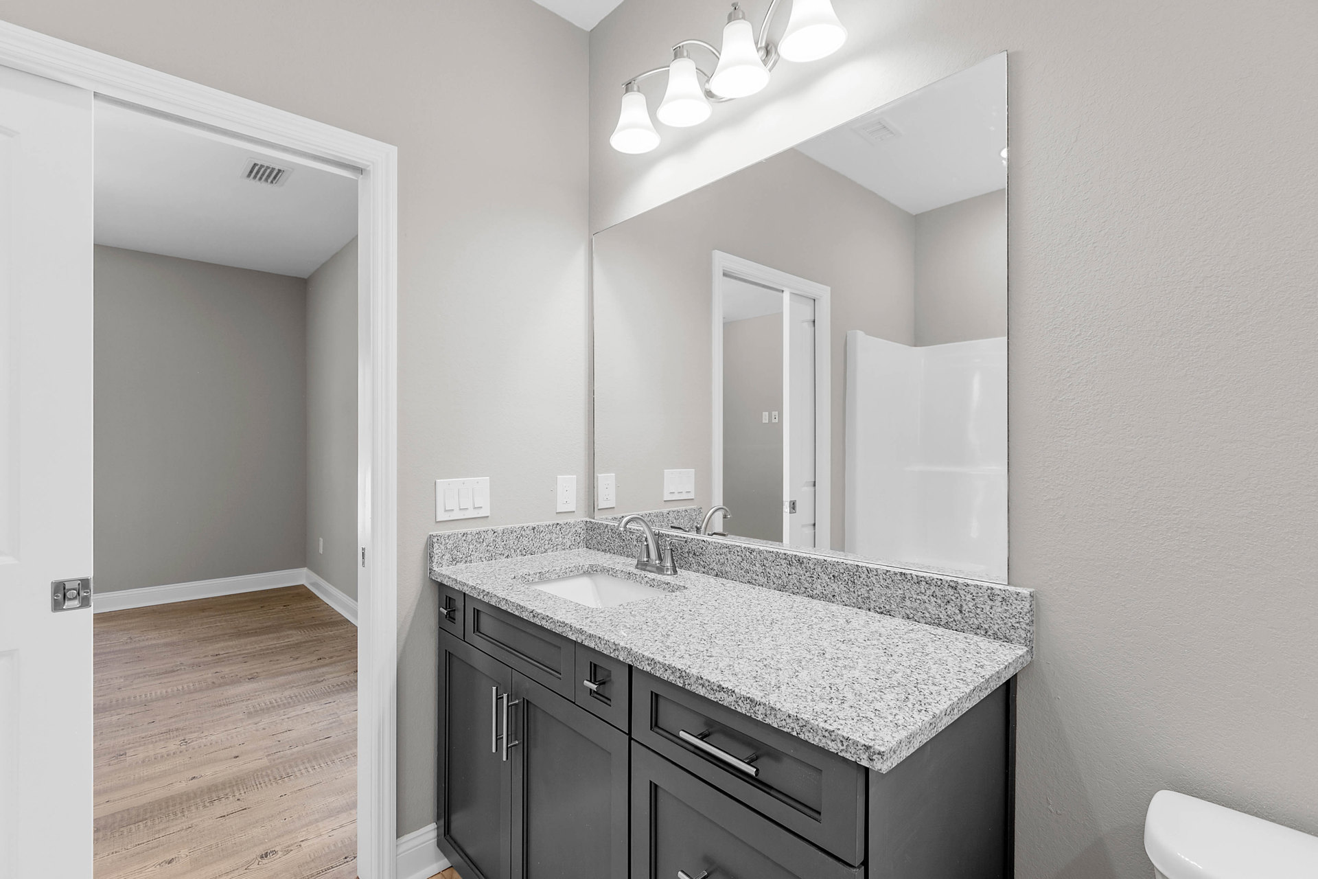Bathroom with a wide mirror above a white sink and dark cabinetry, wood flooring, and modern light fixture