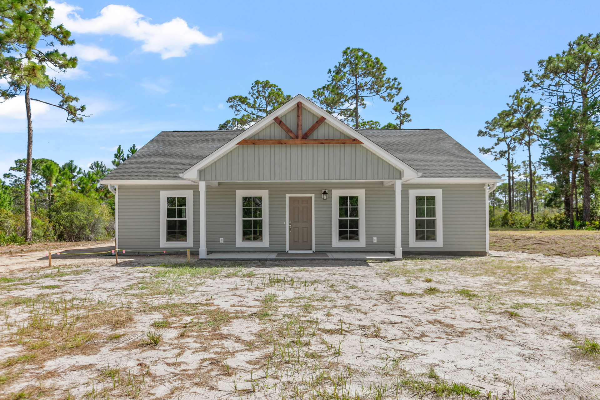 Two-story home with brown front door, white-framed windows, gray roof, surrounded by dirt yard and mature trees