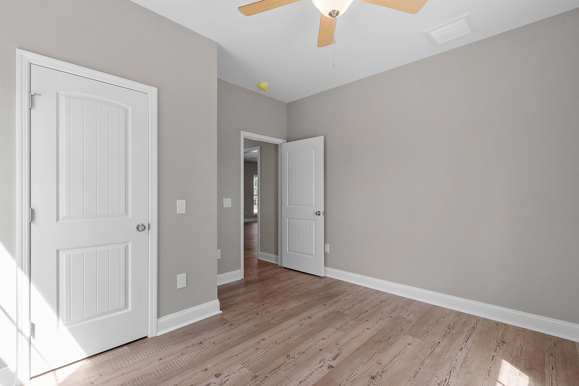 Room with wood laminate flooring, white door with silver handle, ceiling fan, white walls, and crown molding