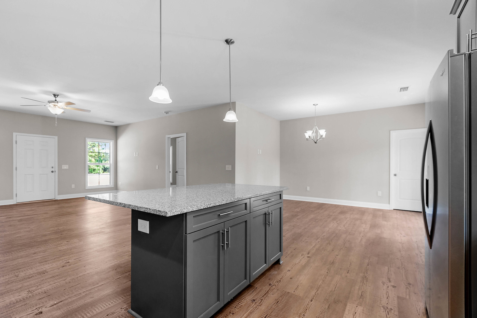 Granite kitchen island with built-in sink, dark cabinetry, wood flooring, white wall with outlet, white door with silver handle, window overlooking trees