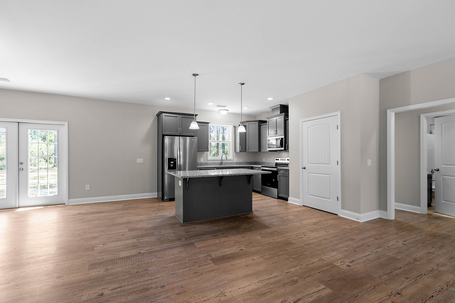 Stainless steel kitchen island with wood flooring, glass-paneled door revealing trees, white door with silver handle, black box on floor, countertop, and close-up stainless