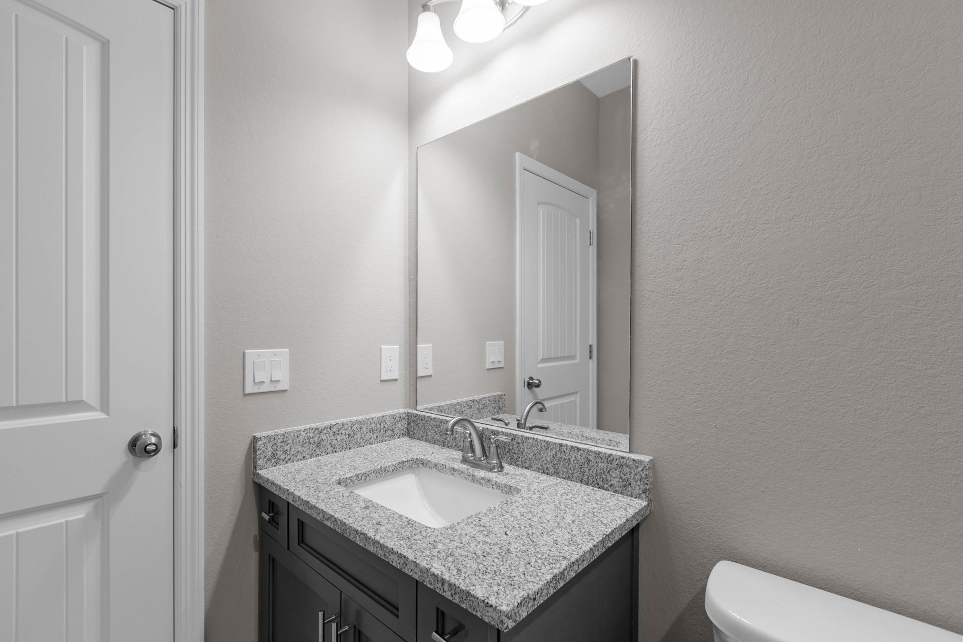 White quartz countertop with undermount sink, chrome faucet, large frameless mirror, light gray tile backsplash, white cabinetry, and brushed nickel hardware in a modern bathroom