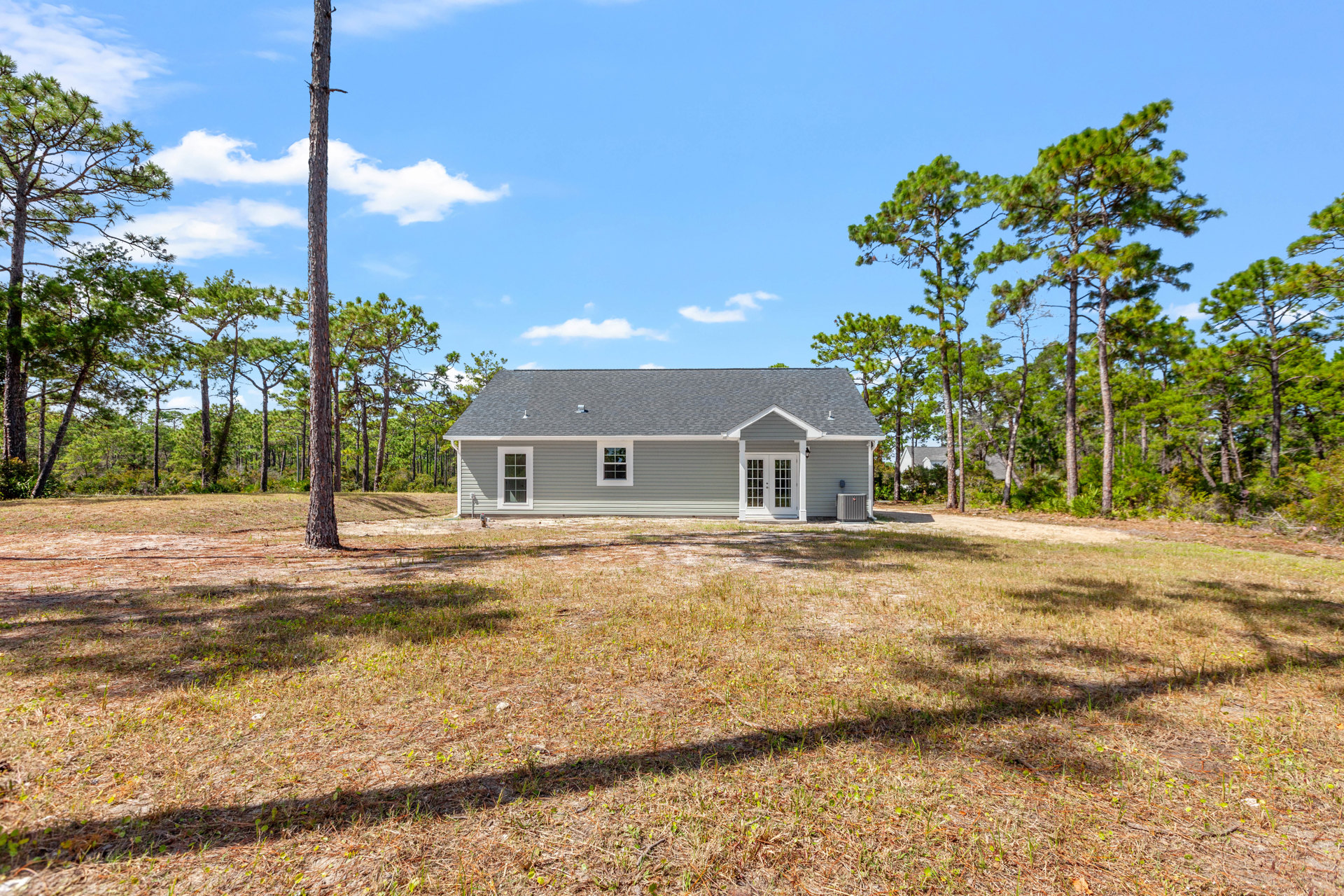 Two-story farmhouse with white double doors, large windows, manicured lawn, mature trees and blue sky in the background