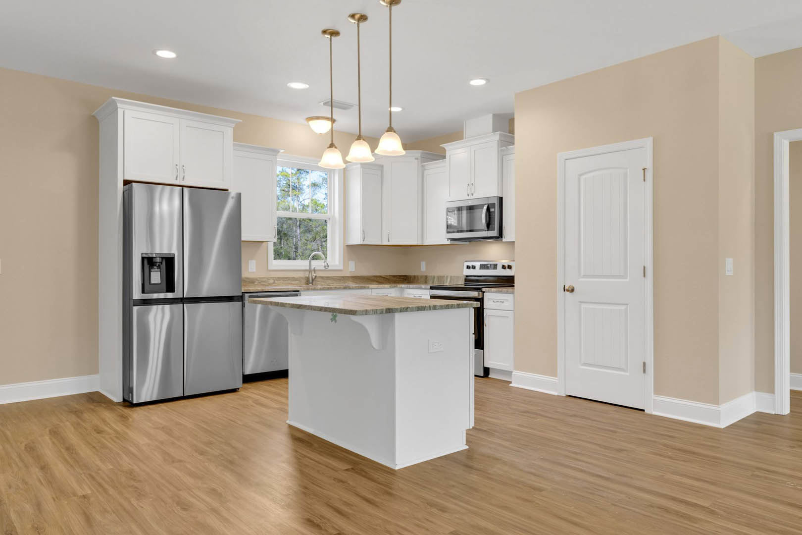 White kitchen island with marble countertop, stainless steel refrigerator and microwave, gold handle on white door, modern cabinetry, faucet over undermount sink