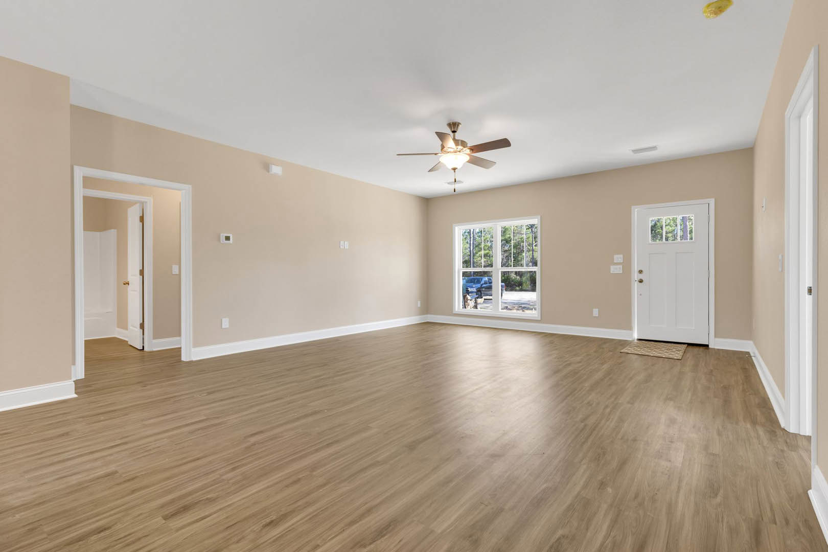 Spacious room with wood flooring, ceiling fan with light, large window overlooking parking lot, and white door with glass inset