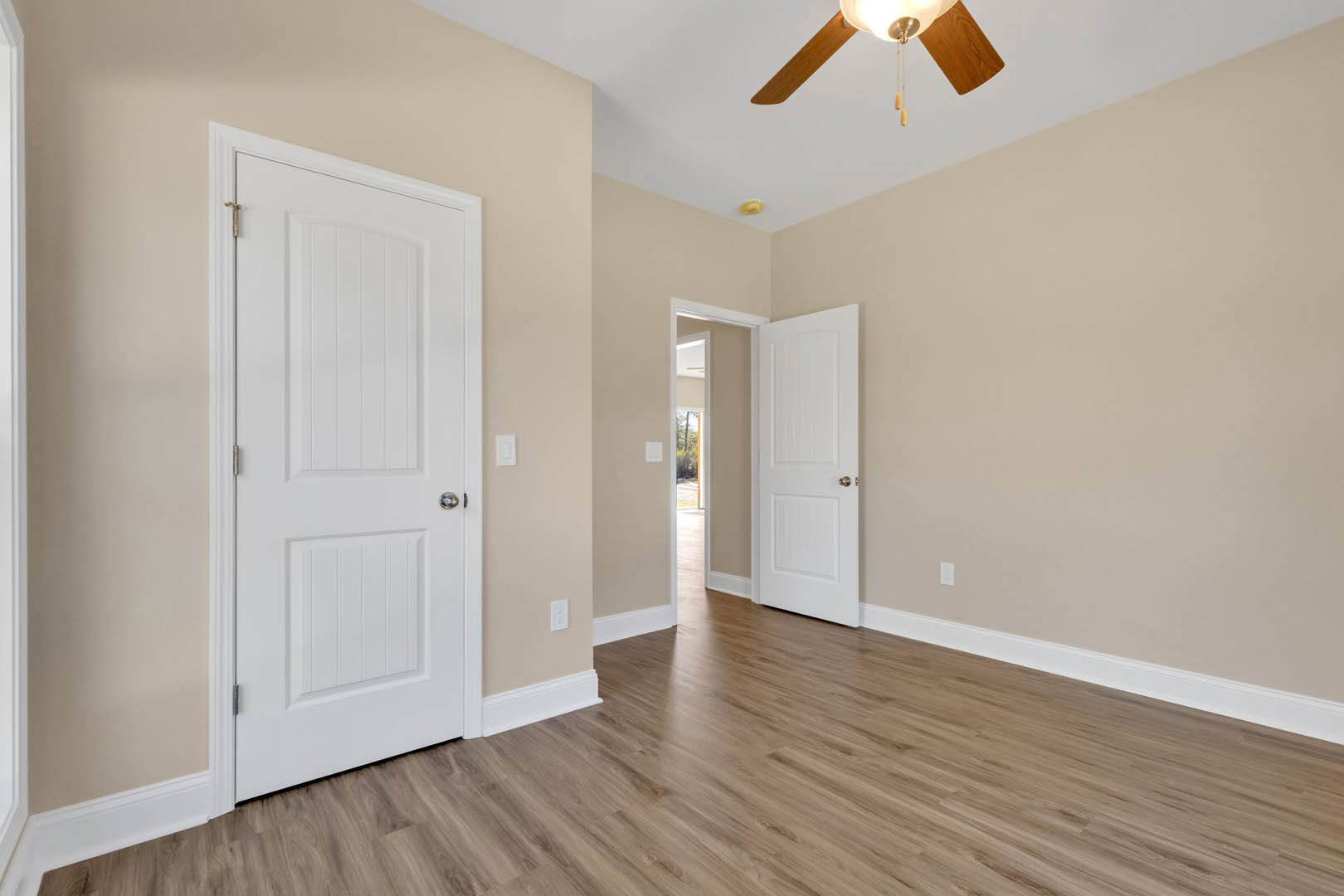 Hardwood floor with white baseboard trim, white paneled doors featuring silver knobs, ceiling fan with central light fixture, white cabinetry against neutral plaster walls