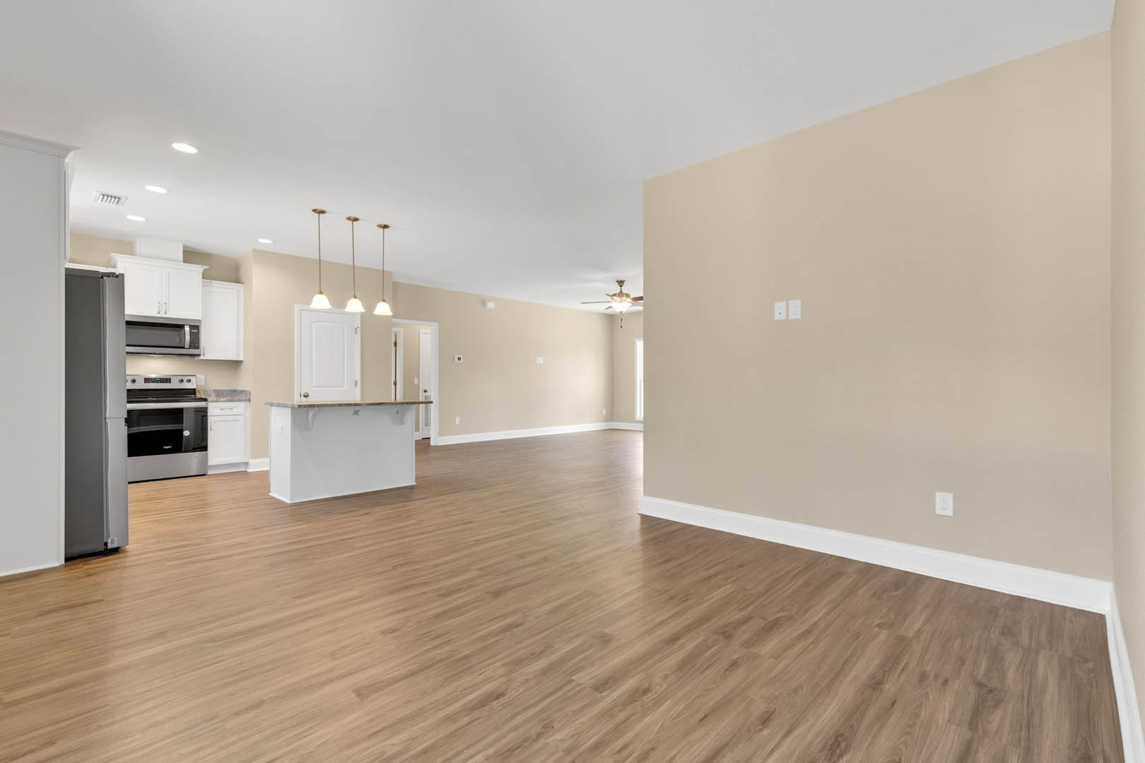 Open kitchen with hardwood flooring, white cabinetry, brown countertop, stainless steel oven, and row of ceiling lights against white walls