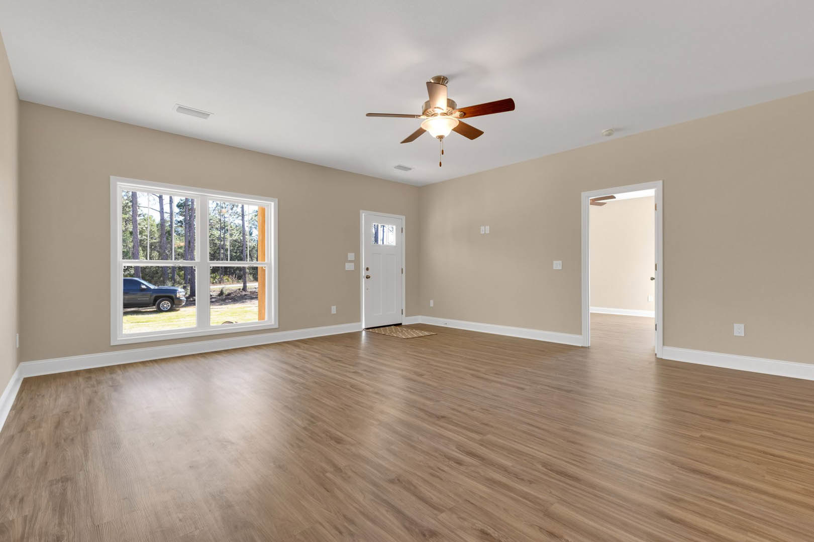 Ceiling fan with light fixture, hardwood flooring, white door with window, large window showing parked black truck outside, neutral plaster walls