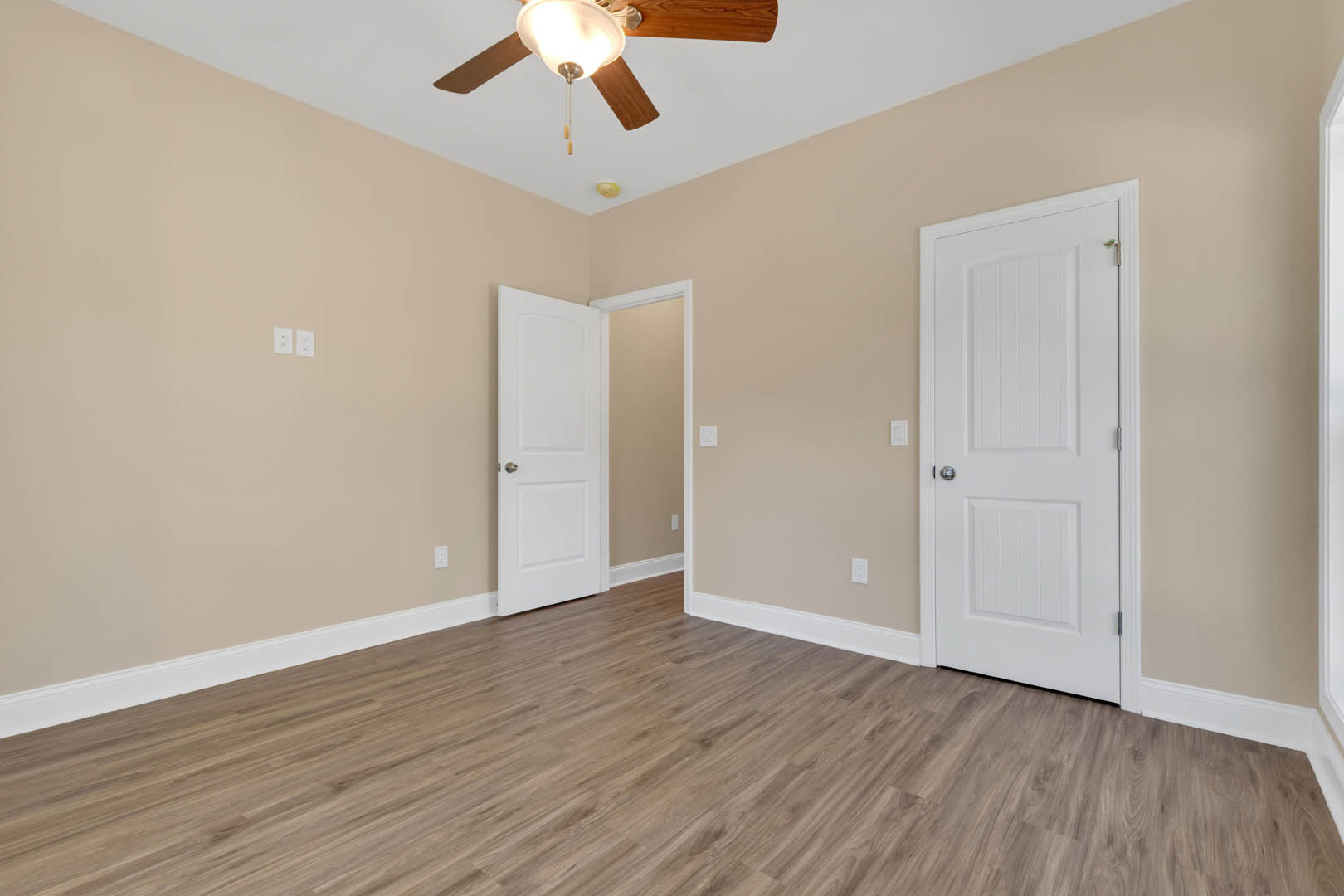 Wood flooring with white trim, ceiling fan and light fixture, two white doors with silver handles, white walls and door frames