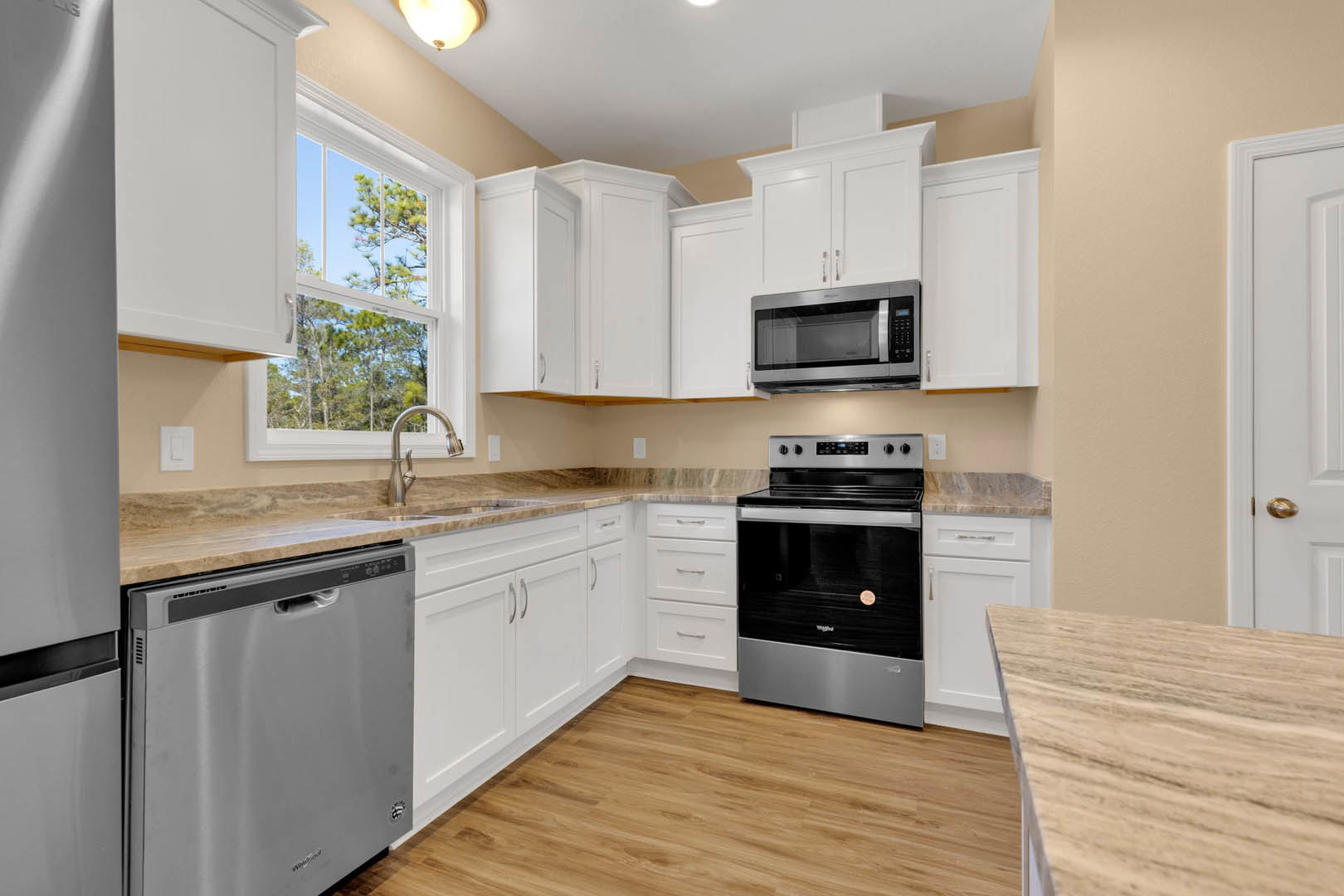 White shaker cabinets, black freestanding stove, stainless microwave with glass door, integrated dishwasher, quartz countertops, pendant light fixture, wood dining table in