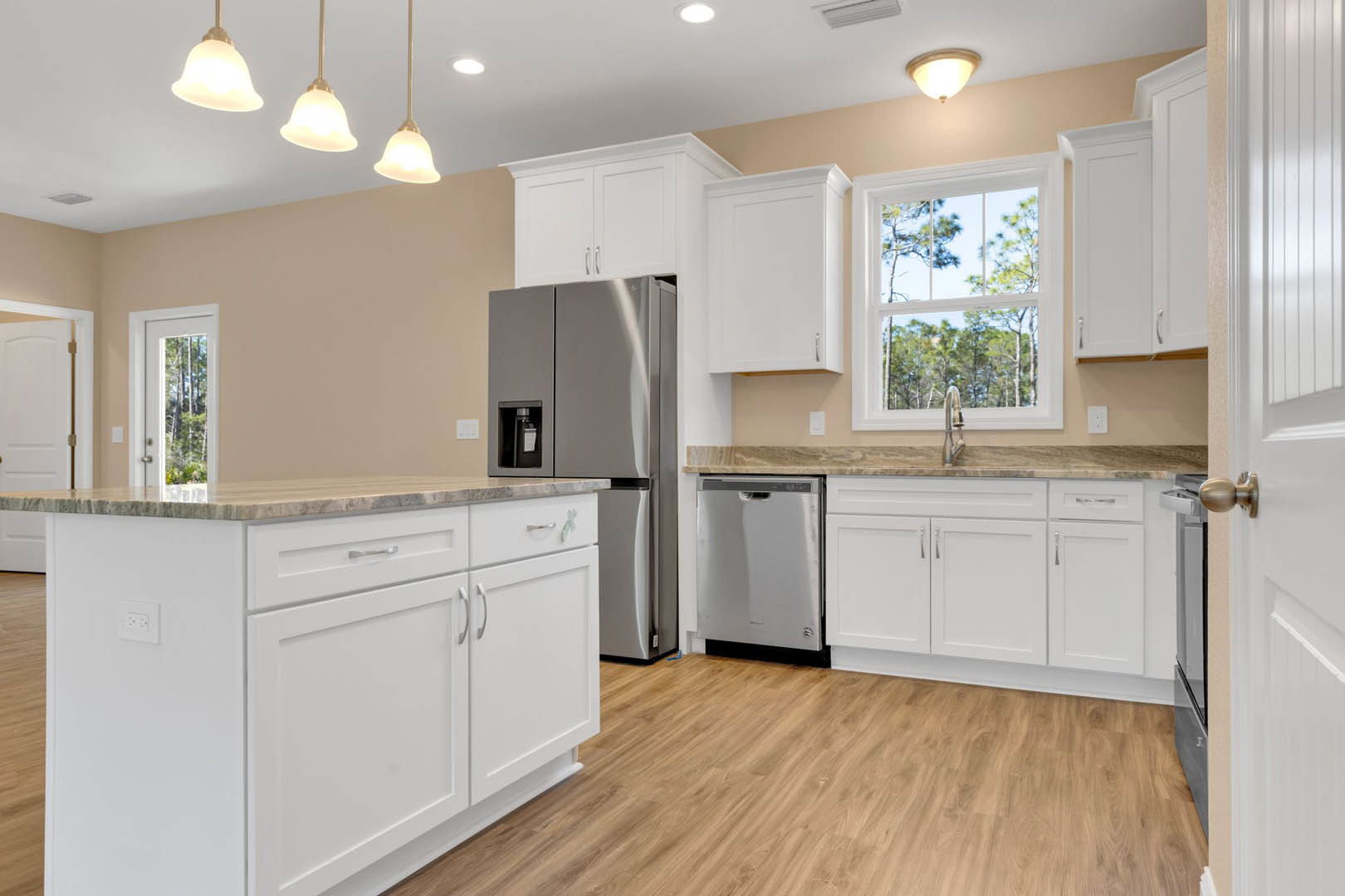 White kitchen with shaker cabinets, stainless steel refrigerator, marble island countertop, wood flooring, and a window above the sink.